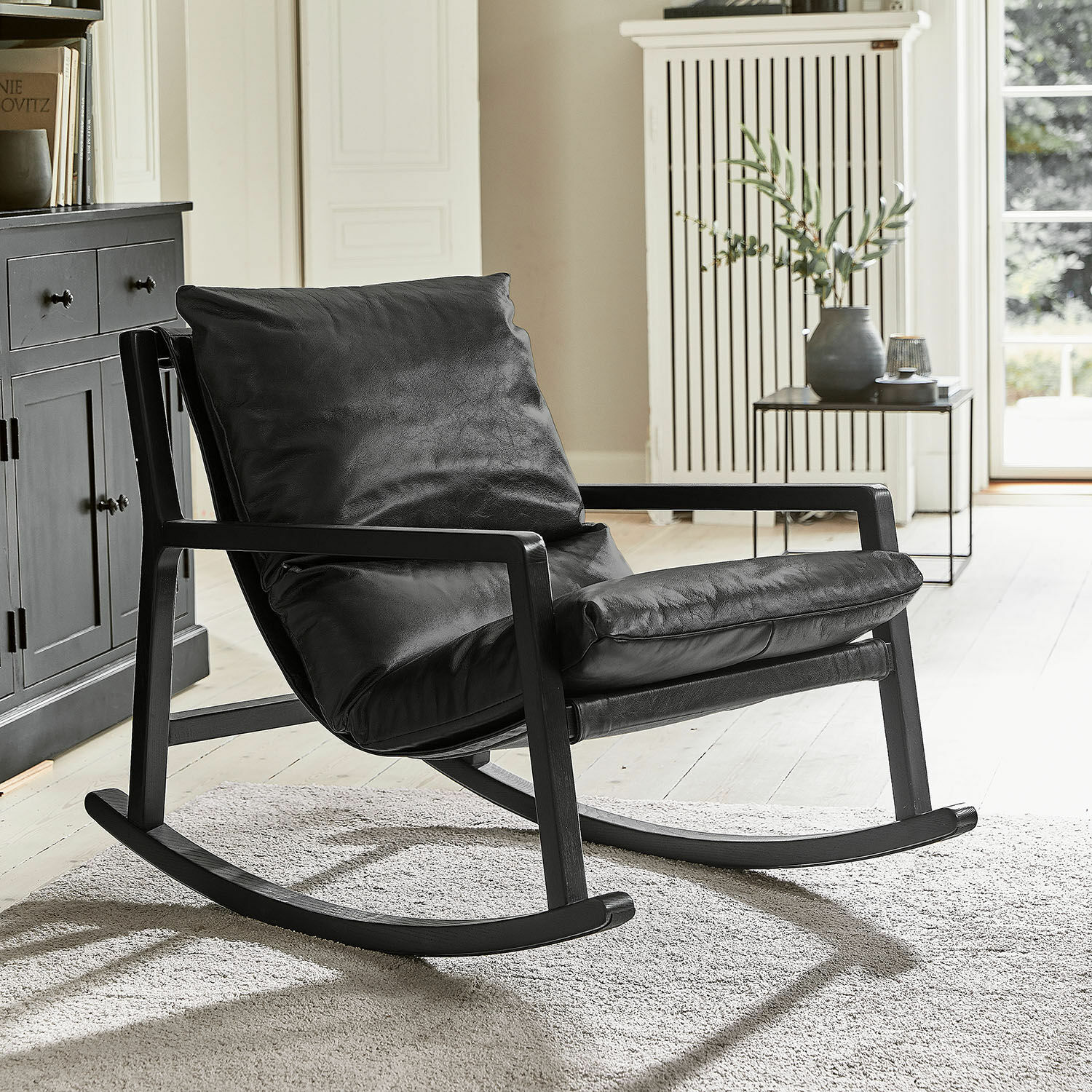 Schommelstoel Falconridge Zwarte schommelstoel van zacht leer met houten frame in moderne woonkamer