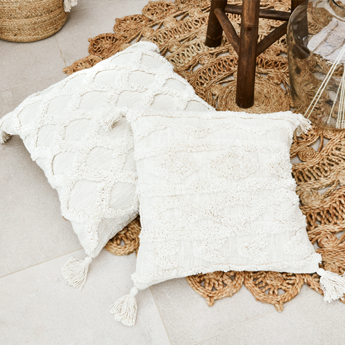 Deux coussins décoratifs crème en coton avec pompons aux coins sur un tapis tressé