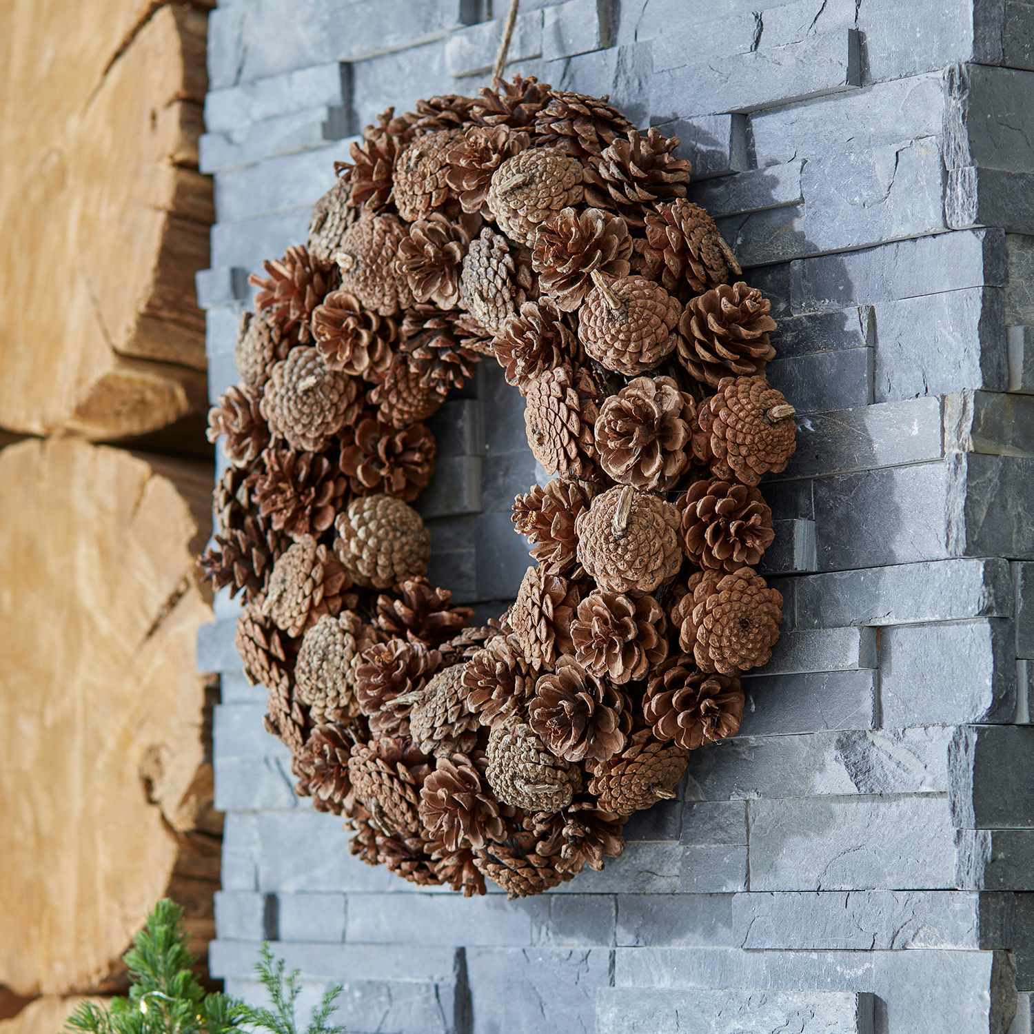 Couronne Mellor Couronne décorative en pommes de pin naturelles marron sur un mur en pierre grise