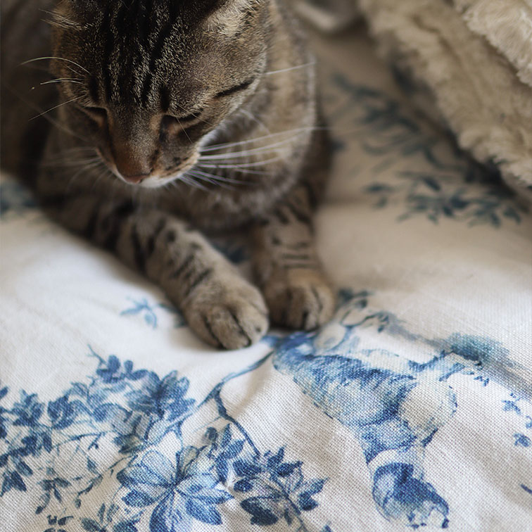 Chat tigré gris sur tissu blanc à motif floral bleu, décoration douce pour intérieur