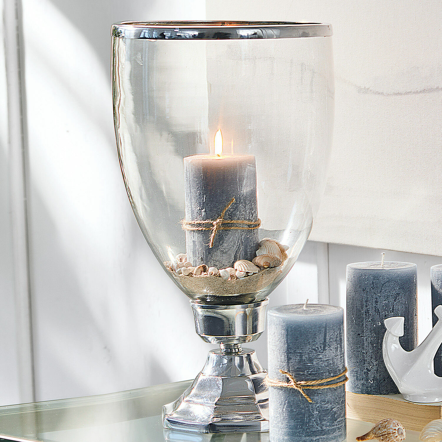 Bougeoir Echelon Bougie grise avec corde en jute dans un photophore en verre avec coquillages et sable sur table