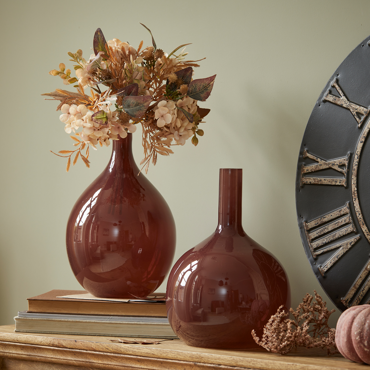 Deux vases décoratifs en verre bordeaux sur une table en bois avec fleurs séchées et livres
