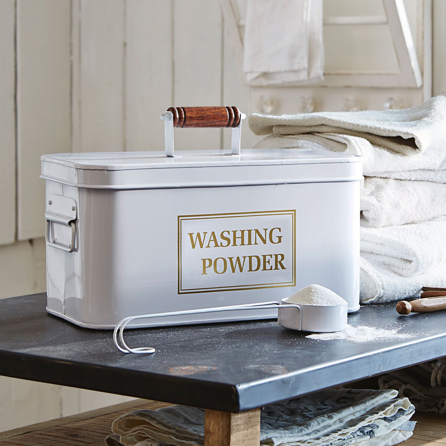 Witte metalen waspoedercontainer met houten handvat en maatlepel op tafel