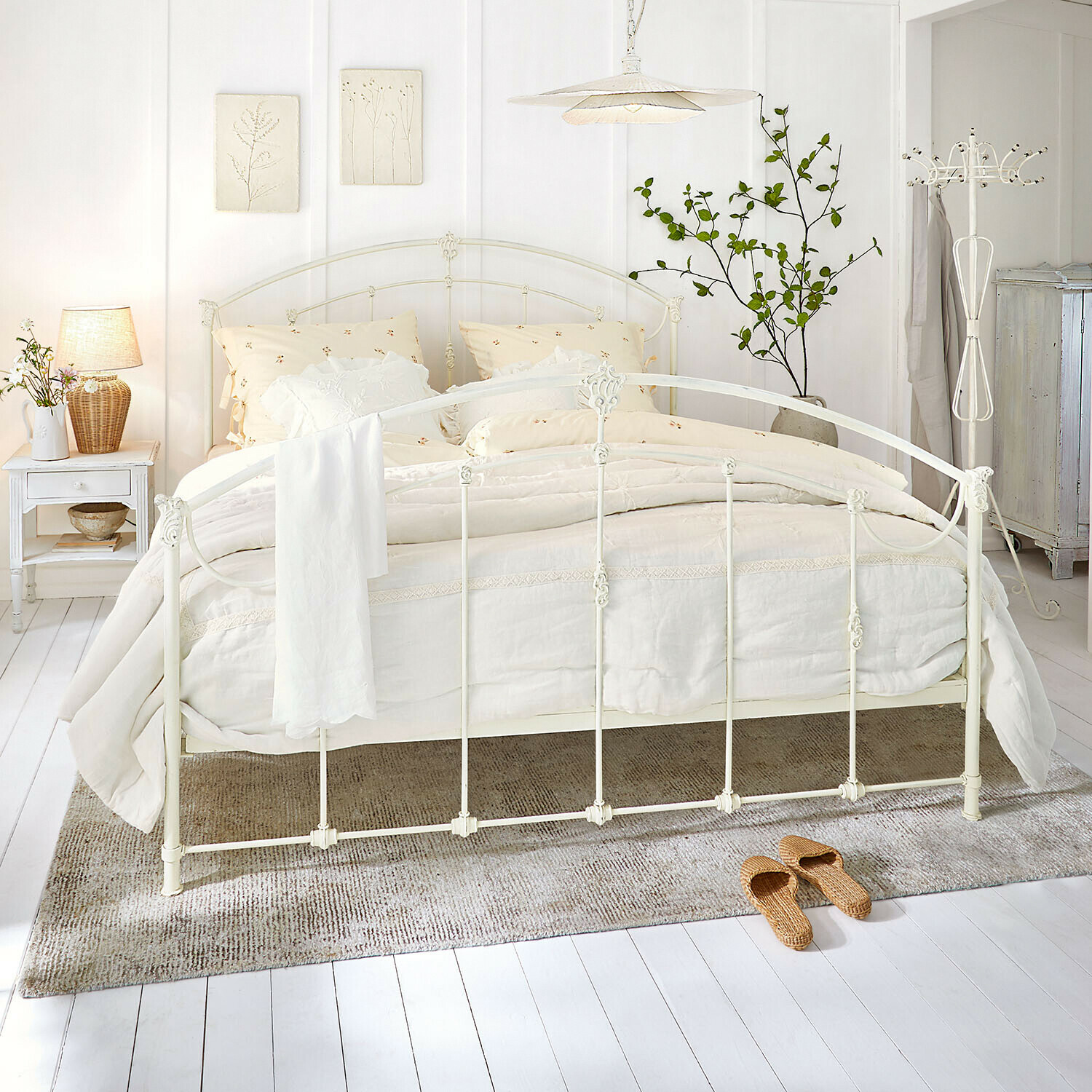 Bed Canefield Witte metalen bedframe met crèmekleurig beddengoed en natuurlijke vloerkleed in lichte slaapkamer
