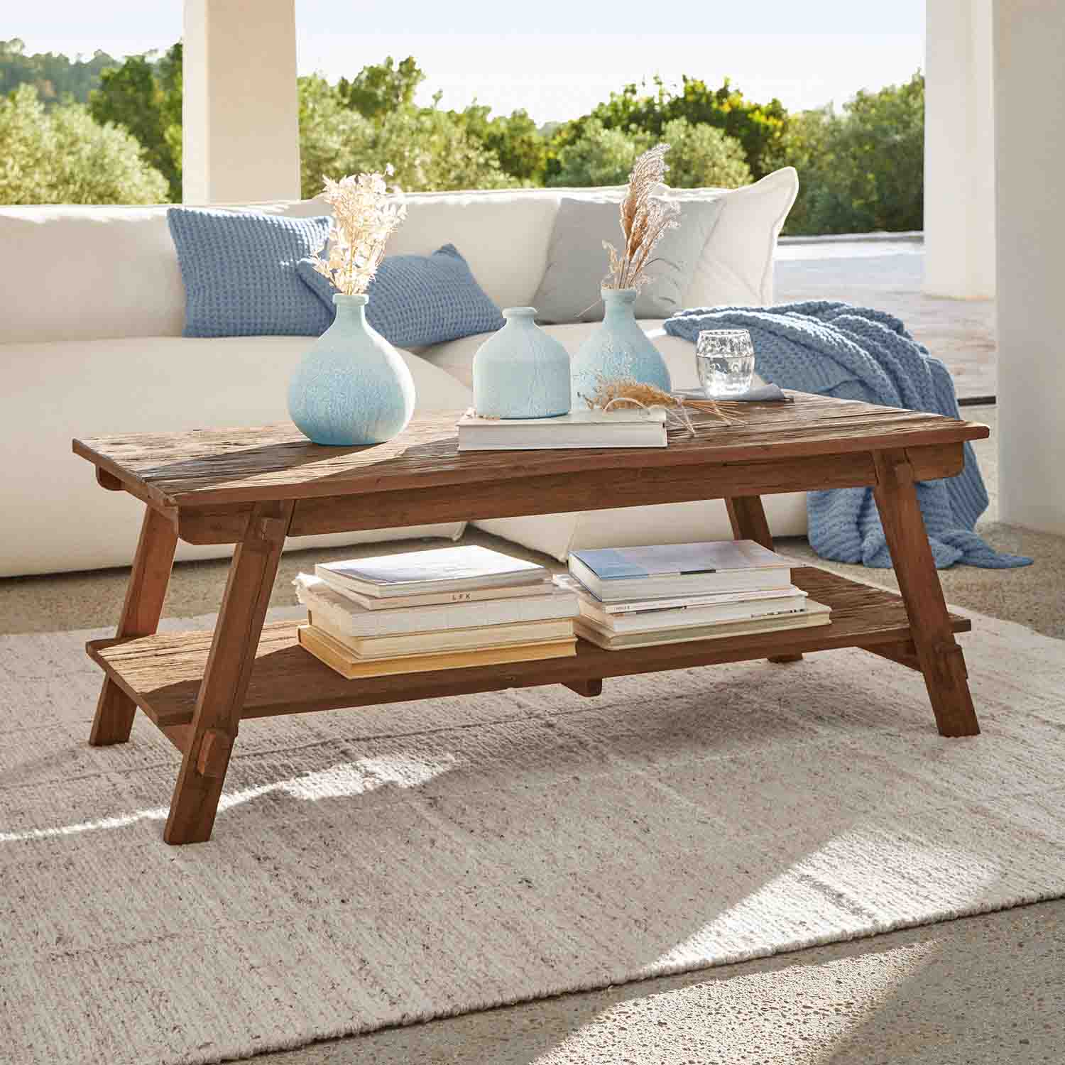 Table basse en bois d'acacia brun avec étagère et vases décoratifs bleus dans un salon lumineux
