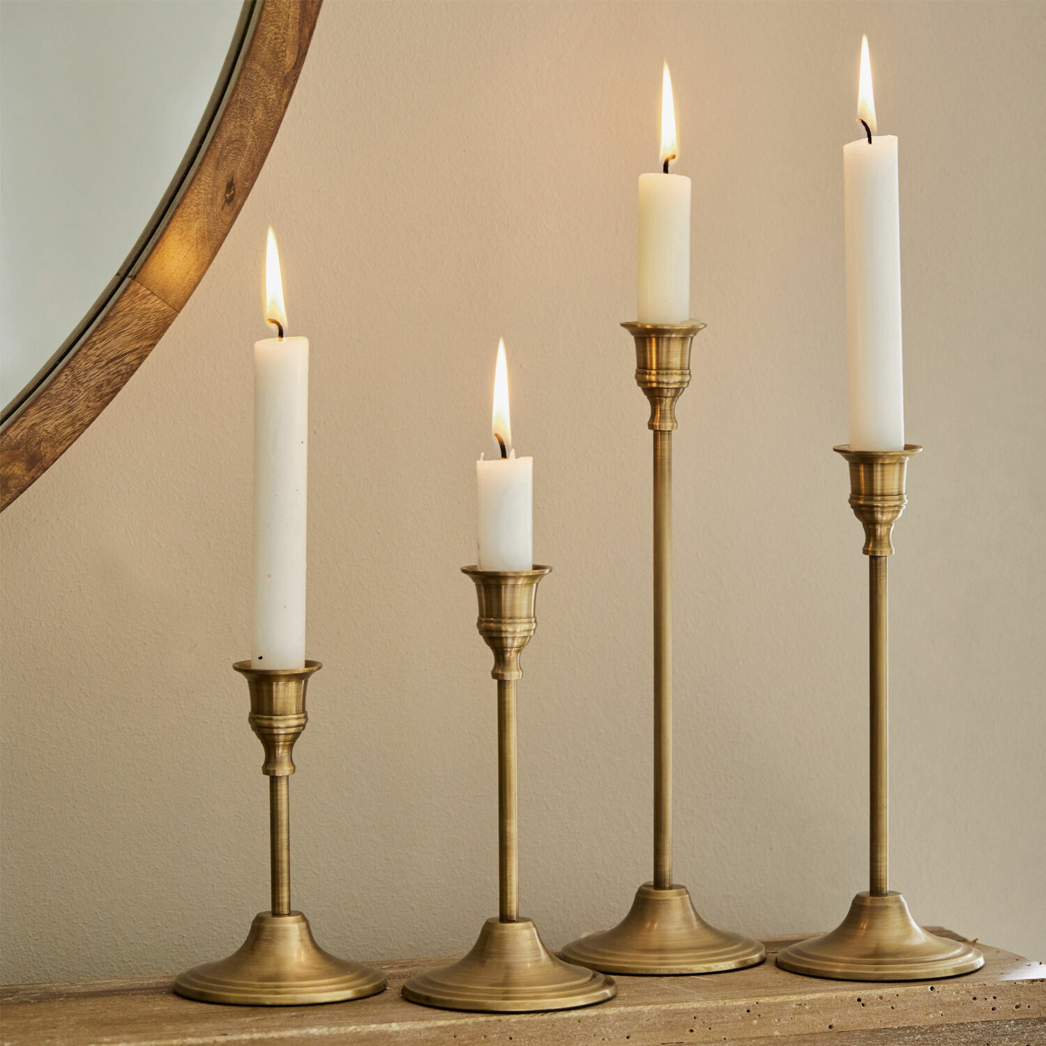 Lot de 4 bougeoirs Namoris Ensemble de quatre bougeoirs en laiton avec bougies blanches sur une surface en bois, décoration intérieure