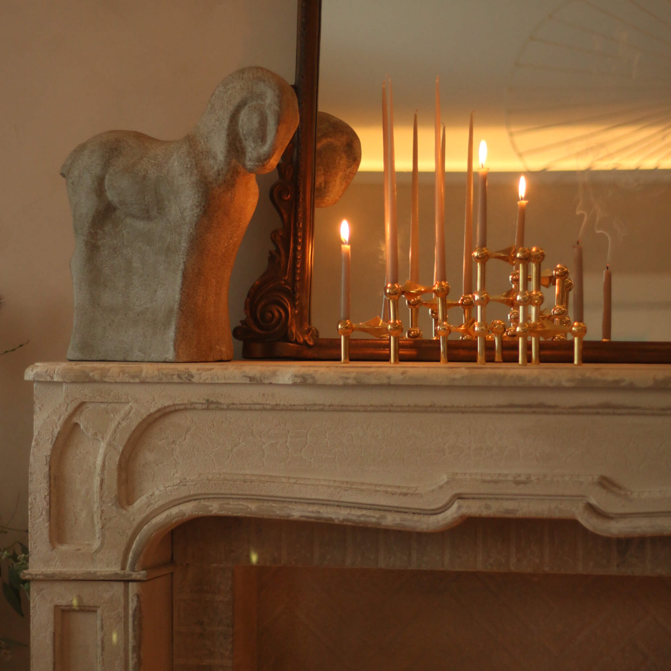 Sculpture décorative de bélier en pierre sur une cheminée avec chandelier en laiton et bougies allumées