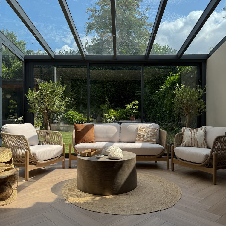 Gezellige woonkamer met lichte houten en stoffen banken onder glazen dak, ronde natuurlijke vloerkleed