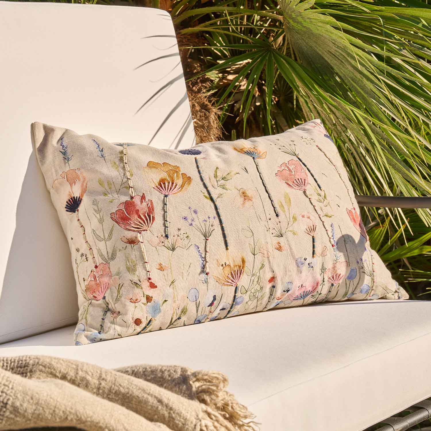 Coussin beige décoratif avec motif floral brodé sur fond clair, parfait pour salon et jardin