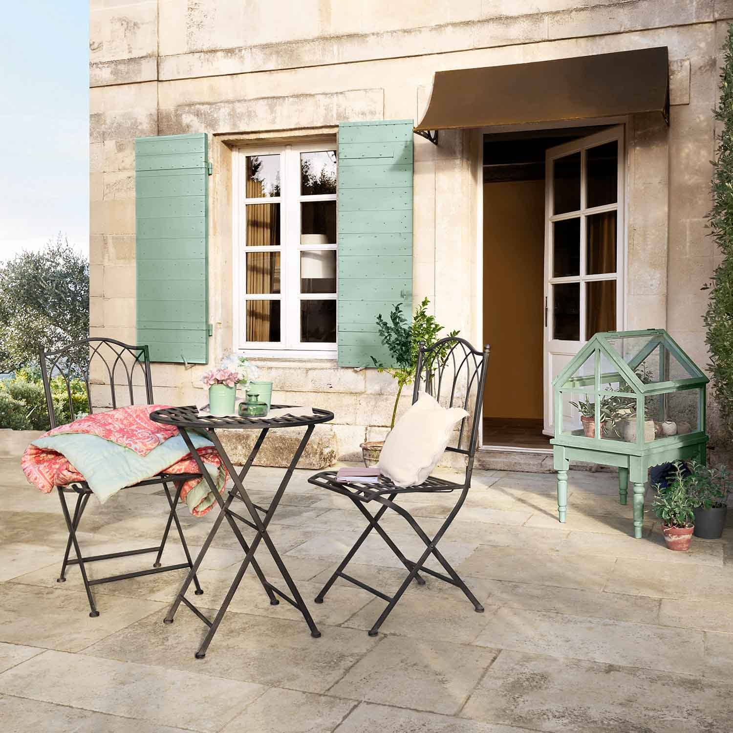 Ensemble de jardin en métal avec table et chaises sur terrasse, mini serre verte et coussins pastel