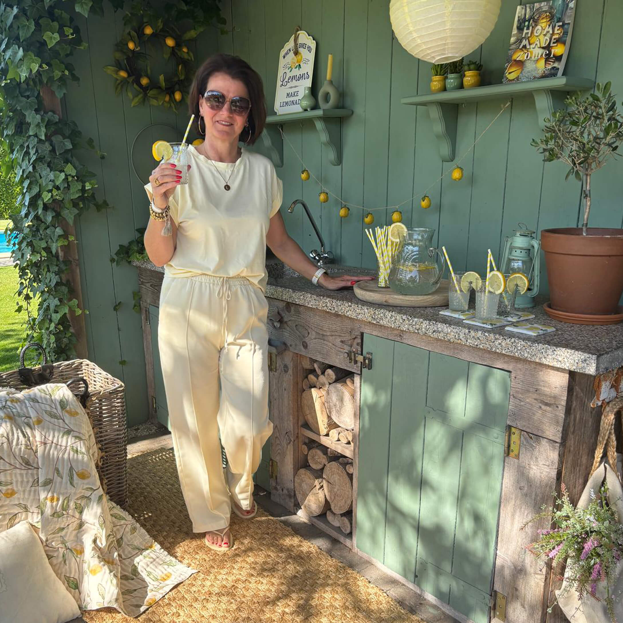 Femme en tenue crème près d'une cuisine extérieure verte avec citronnade et décorations citronnées