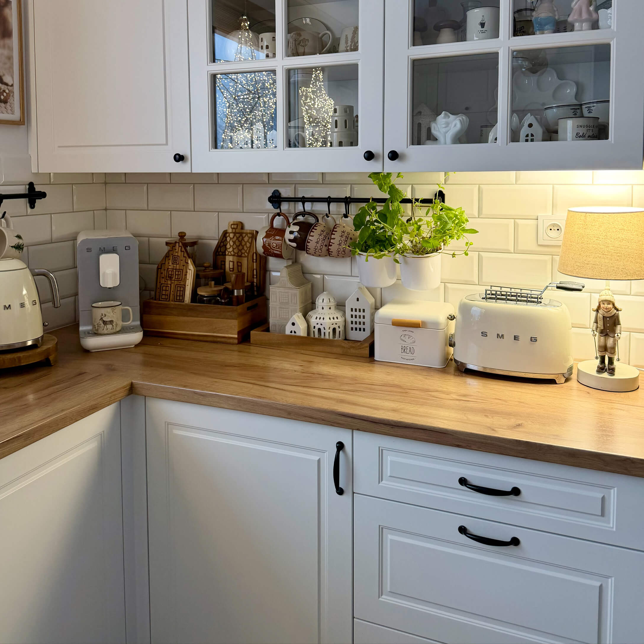 Cuisine avec placards blancs, plan de travail en bois, appareils SMEG crème et décorations avec plantes vertes