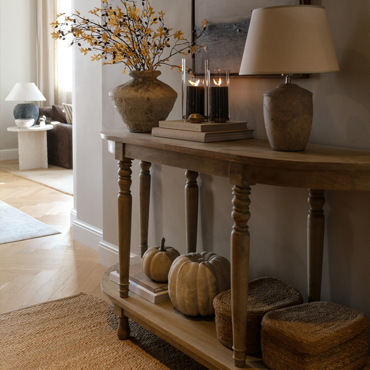 Console en bois avec décorations d'automne, lampe et bougies dans un salon chaleureux aux accents naturels