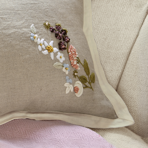 Beige linnen kussen met kleurrijk geborduurd bloemenpatroon en crèmekleurige bies