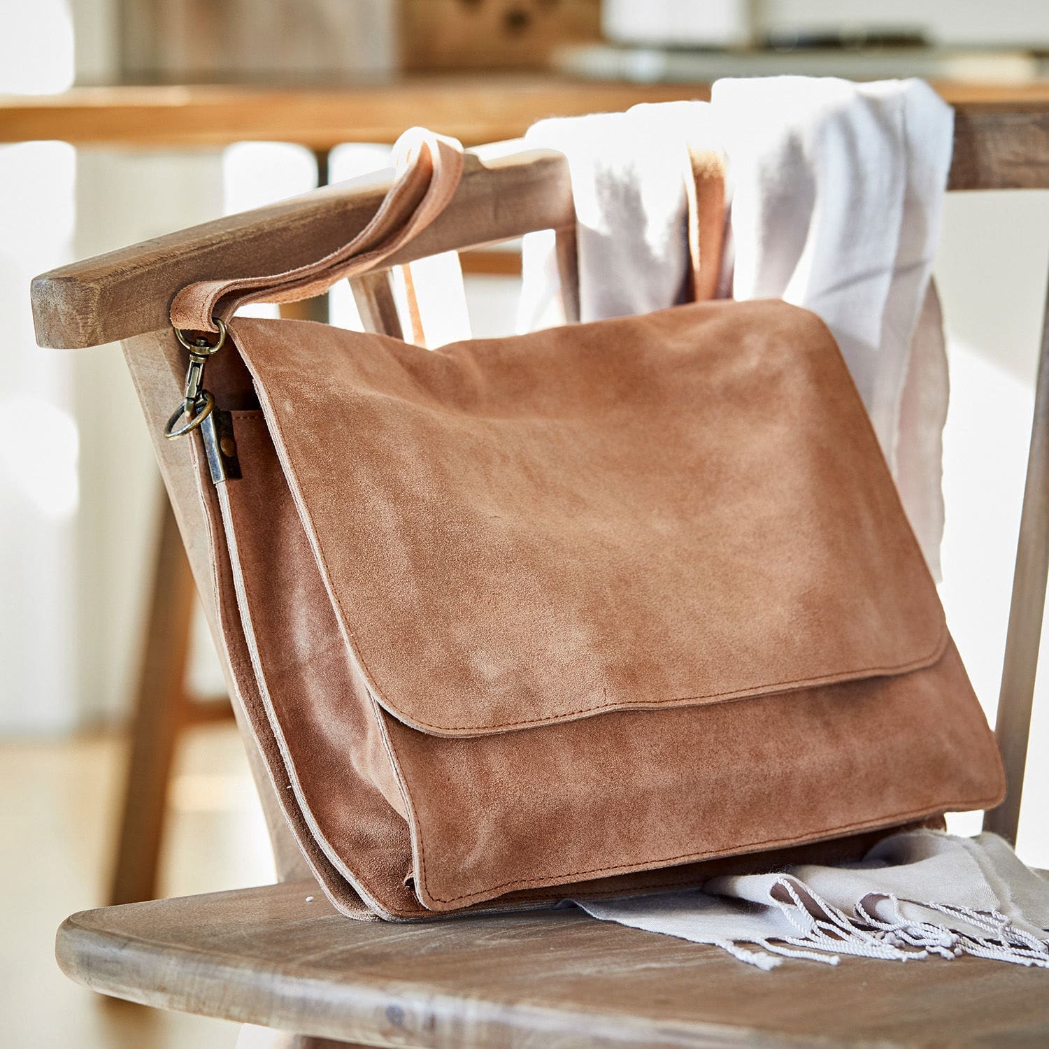 Sac Chanzelle Sac à bandoulière en daim marron posé sur une chaise en bois, accessoire tendance pour un usage quotidien