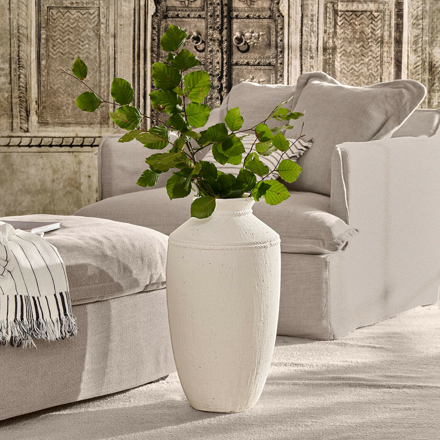 Vaas Niverana Witte keramische vaas met groene bladeren voor een beige bank en decoratieve muur in woonkamer