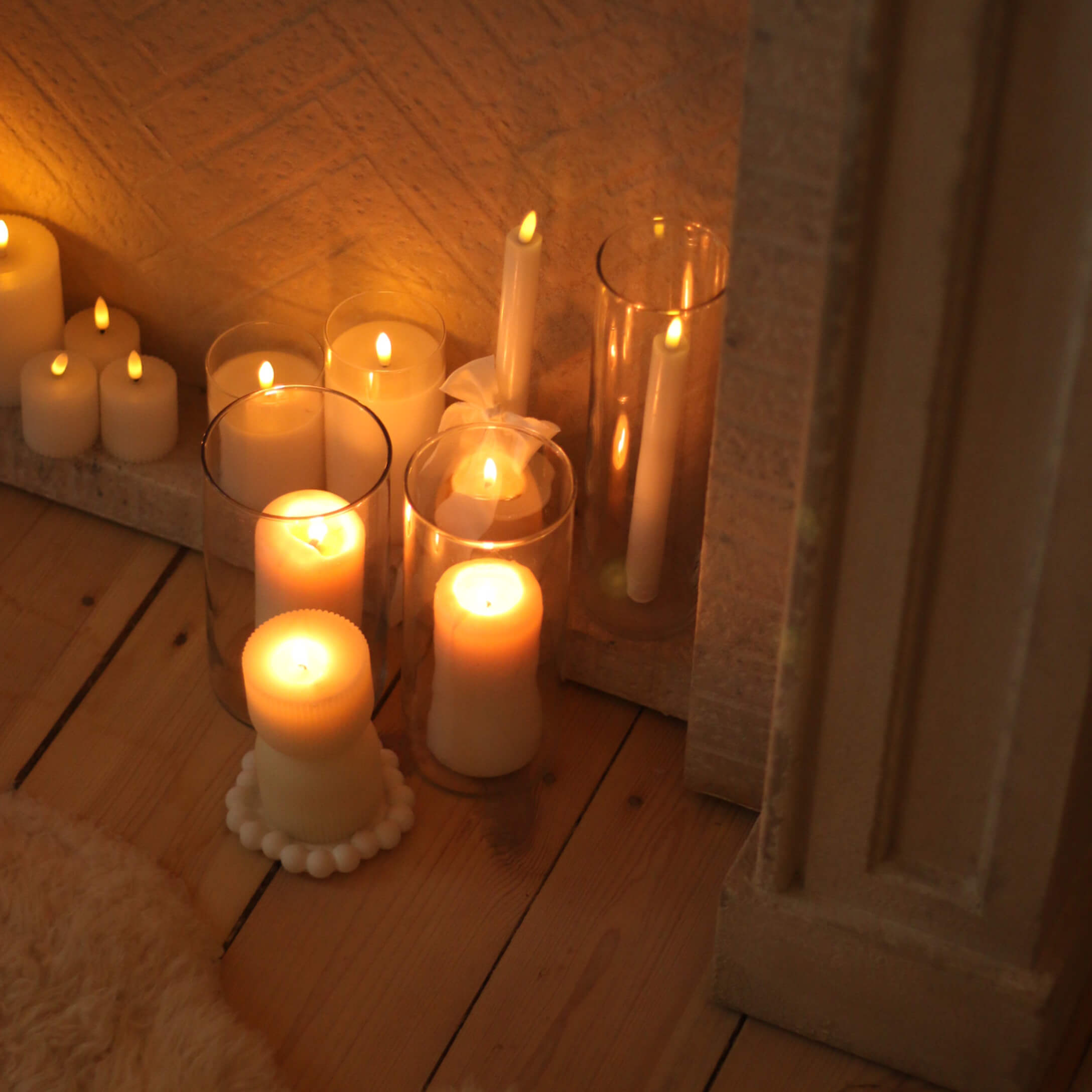 Ensemble de bougies blanches de différentes formes et tailles sur un sol en bois, décoration intérieure