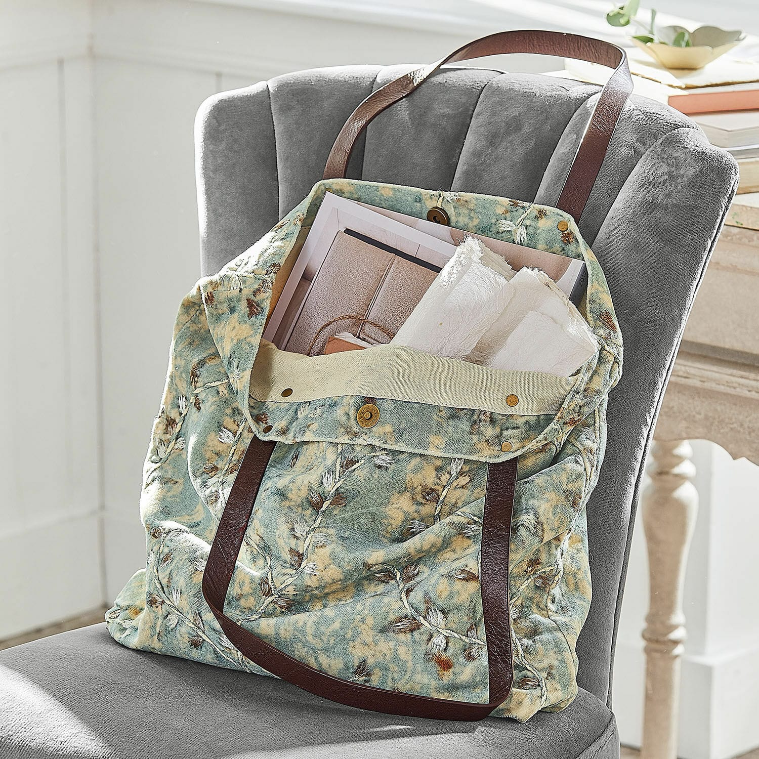 Tas LaRoux Tas van zachte stof met groen-beige patroon en bruine handvatten op een grijze stoel