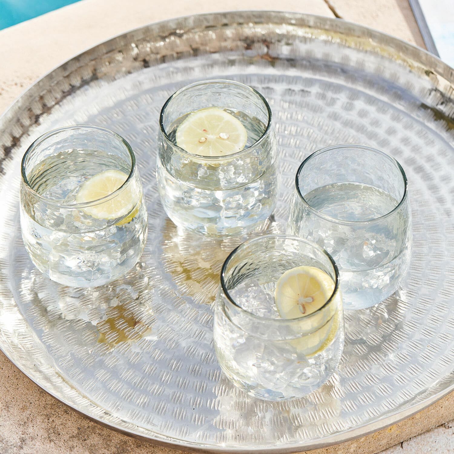 Lot de 4 verres Valters Plateau en métal avec quatre verres d'eau et tranches de citron au bord de la piscine