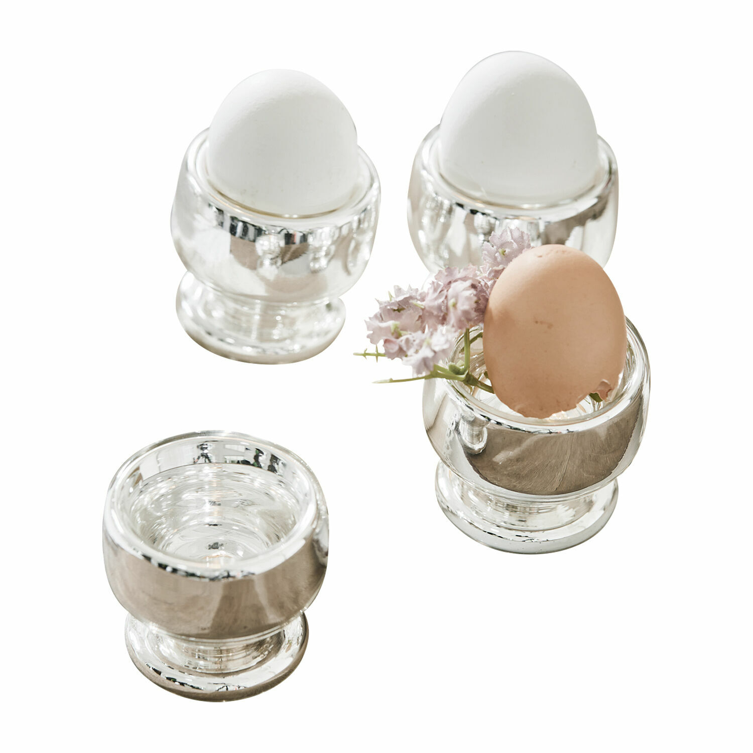 Lot de 4 coquetiers Lilligret Ensemble de quatre porte-œufs en métal argenté avec œufs blancs et bruns et une petite fleur décorative