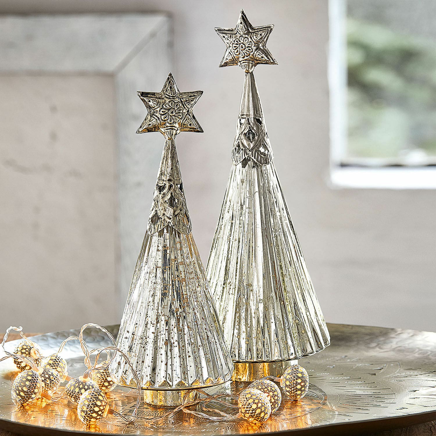 Lot de 2 sapins de Noël décoratifs Lillemor Deux sapins décoratifs en métal argenté avec étoiles au sommet sur une table festive avec guirlande LED