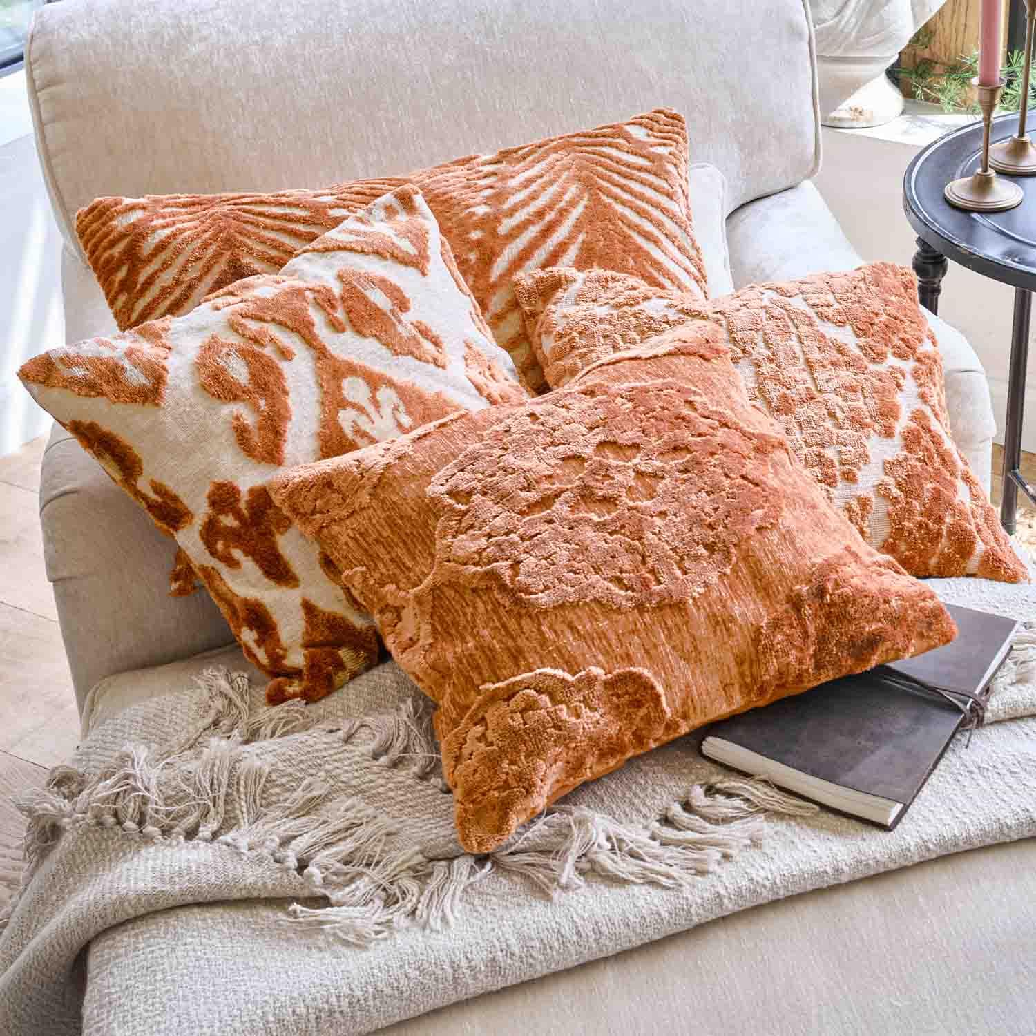 Ensemble de coussins décoratifs orange avec motifs sur canapé clair et plaid à franges