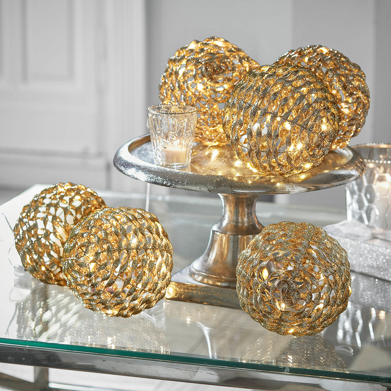 Gouden decoratieve lichtbollen met glitters op een zilveren schaal, sfeervolle feestverlichting