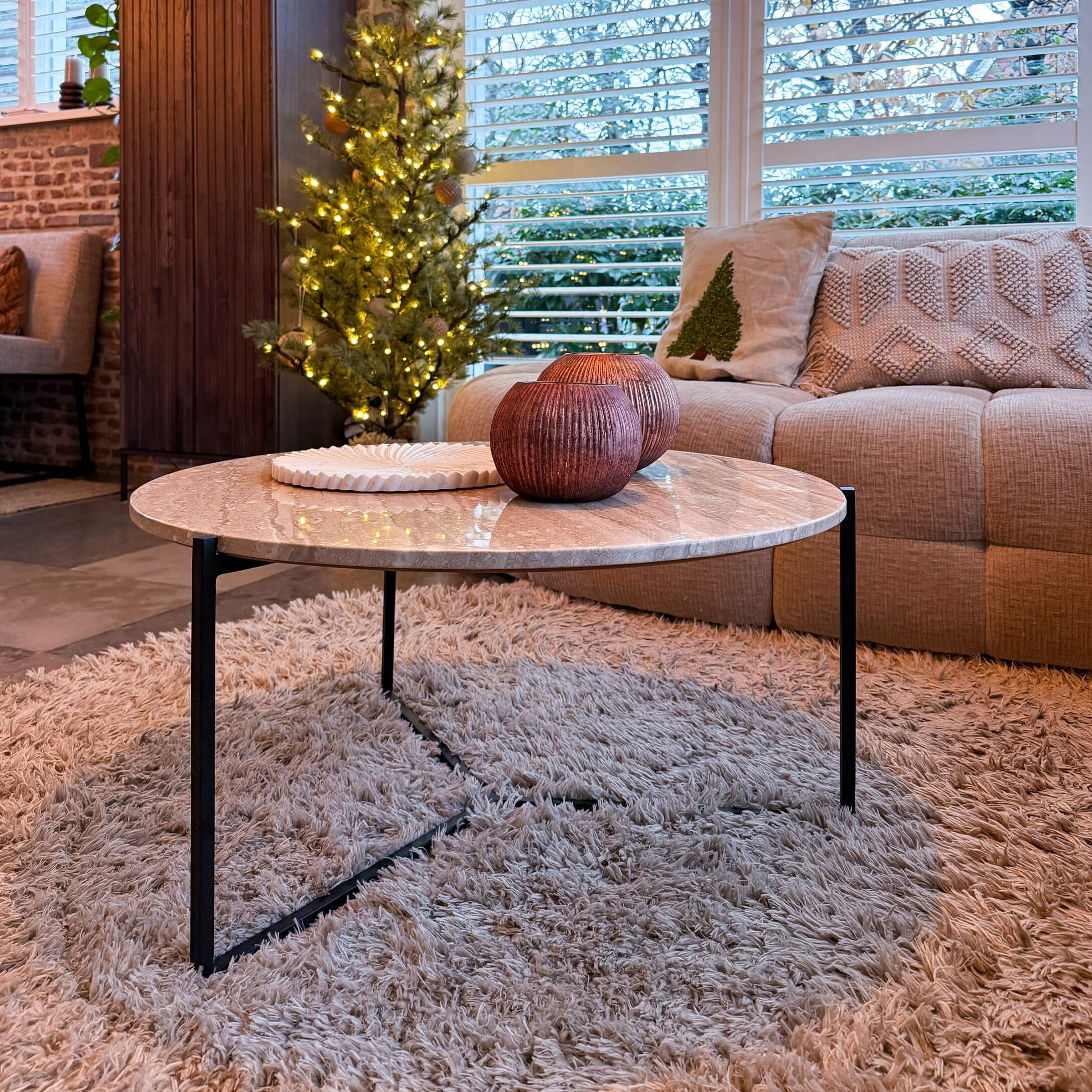 Table basse ronde avec plateau en marbre et pieds en métal noir sur tapis moelleux dans un salon