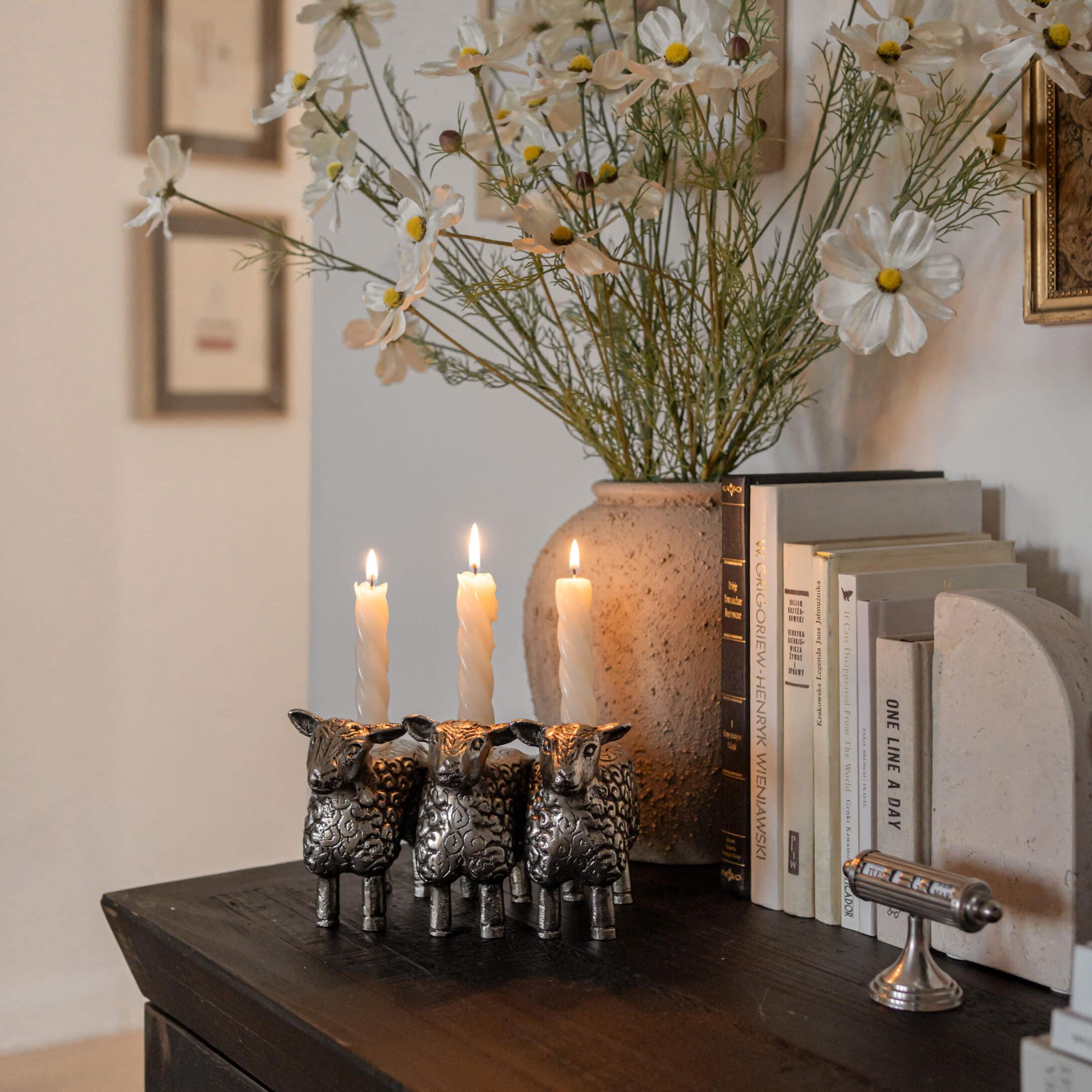 Bougeoir en métal en forme de trois moutons avec des bougies blanches sur une table en bois foncé avec des livres