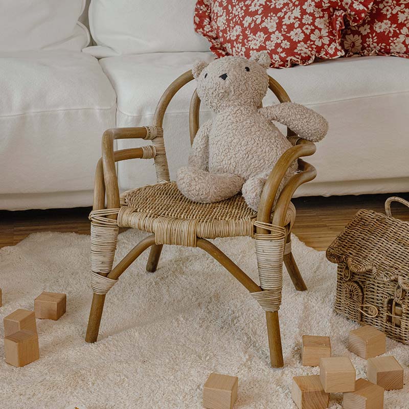 Fauteuil enfant en rotin avec ours en peluche beige sur tapis clair et cubes en bois autour