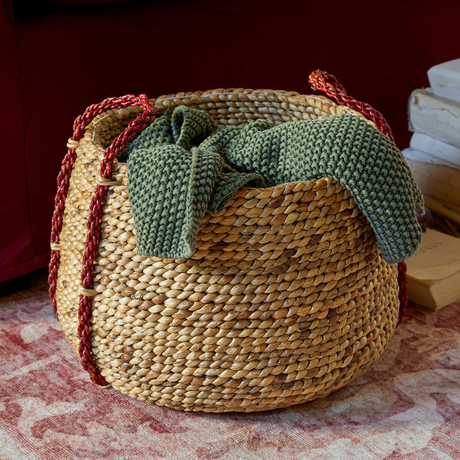 Panier Cilovar Panier rond en osier avec poignées rouges et couverture tricotée verte sur tapis décoratif