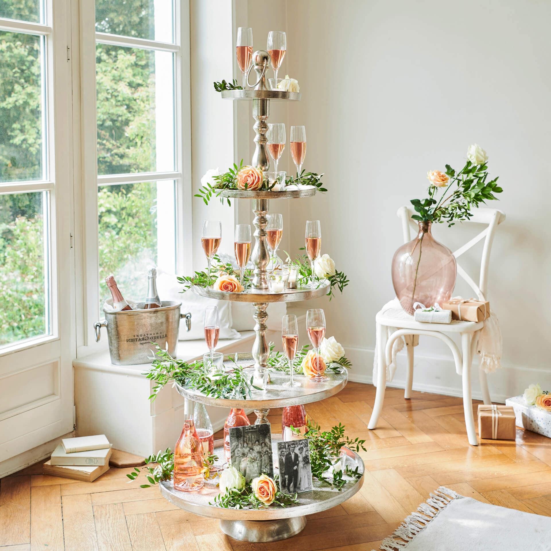 Vierlaagse metalen standaard versierd met rozen en glazen roséwijn in lichte kamer