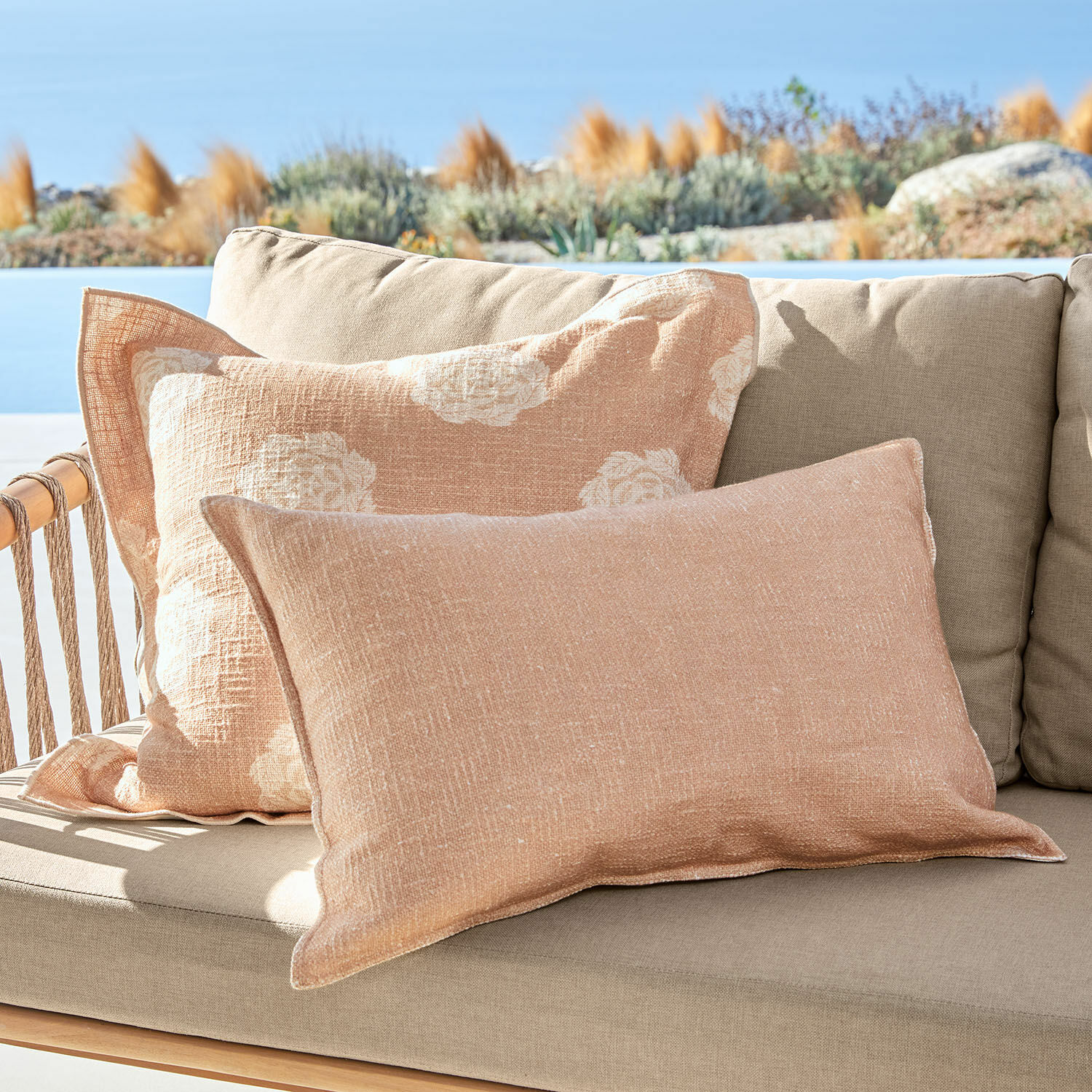 Kussenhoes set van 2 Belvienne Beige linnen sierkussens op beige bank buiten met uitzicht op tuin en lucht