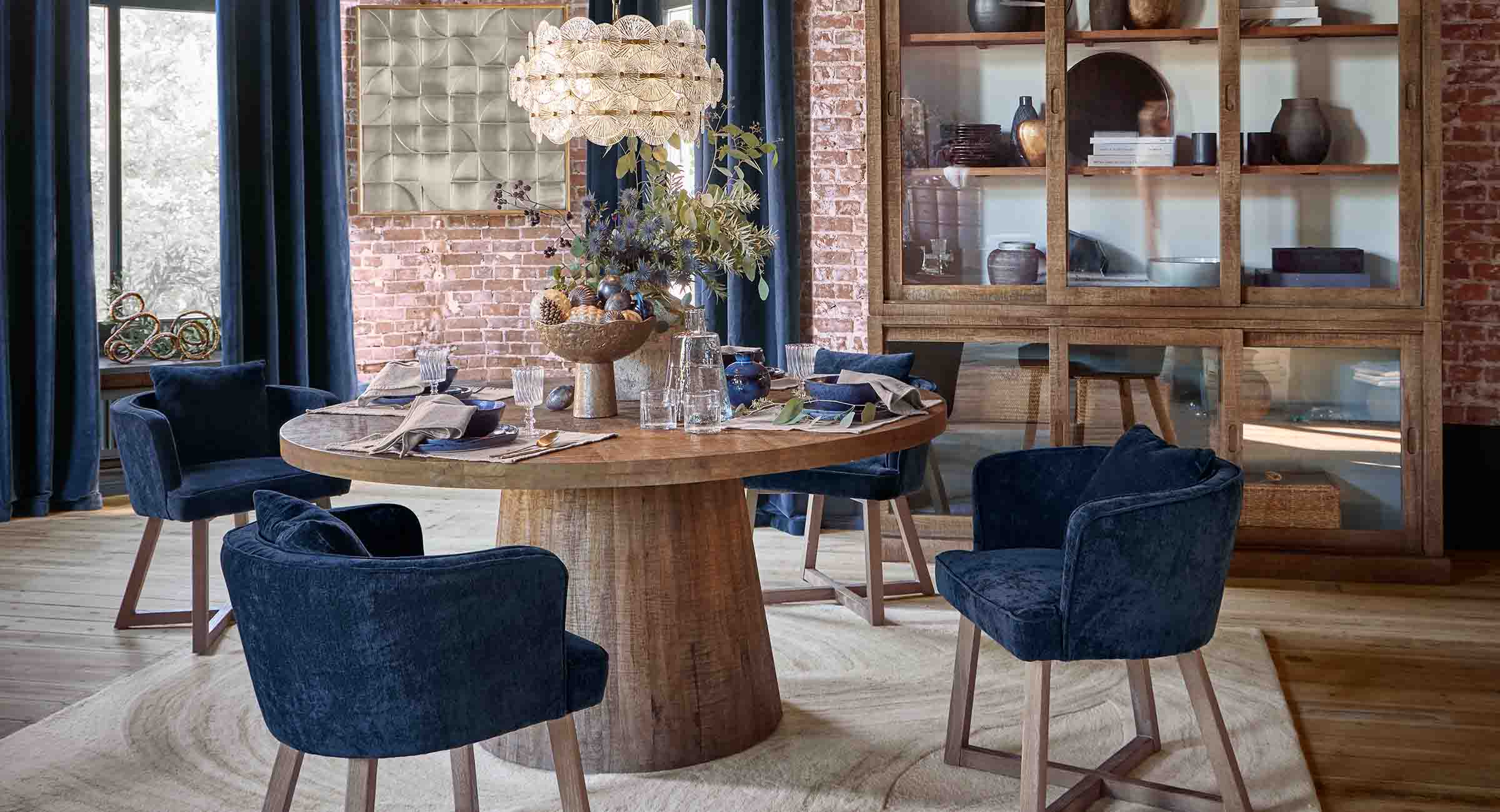 Salle à manger avec table ronde en bois et chaises en velours bleu marine dans un style loft
