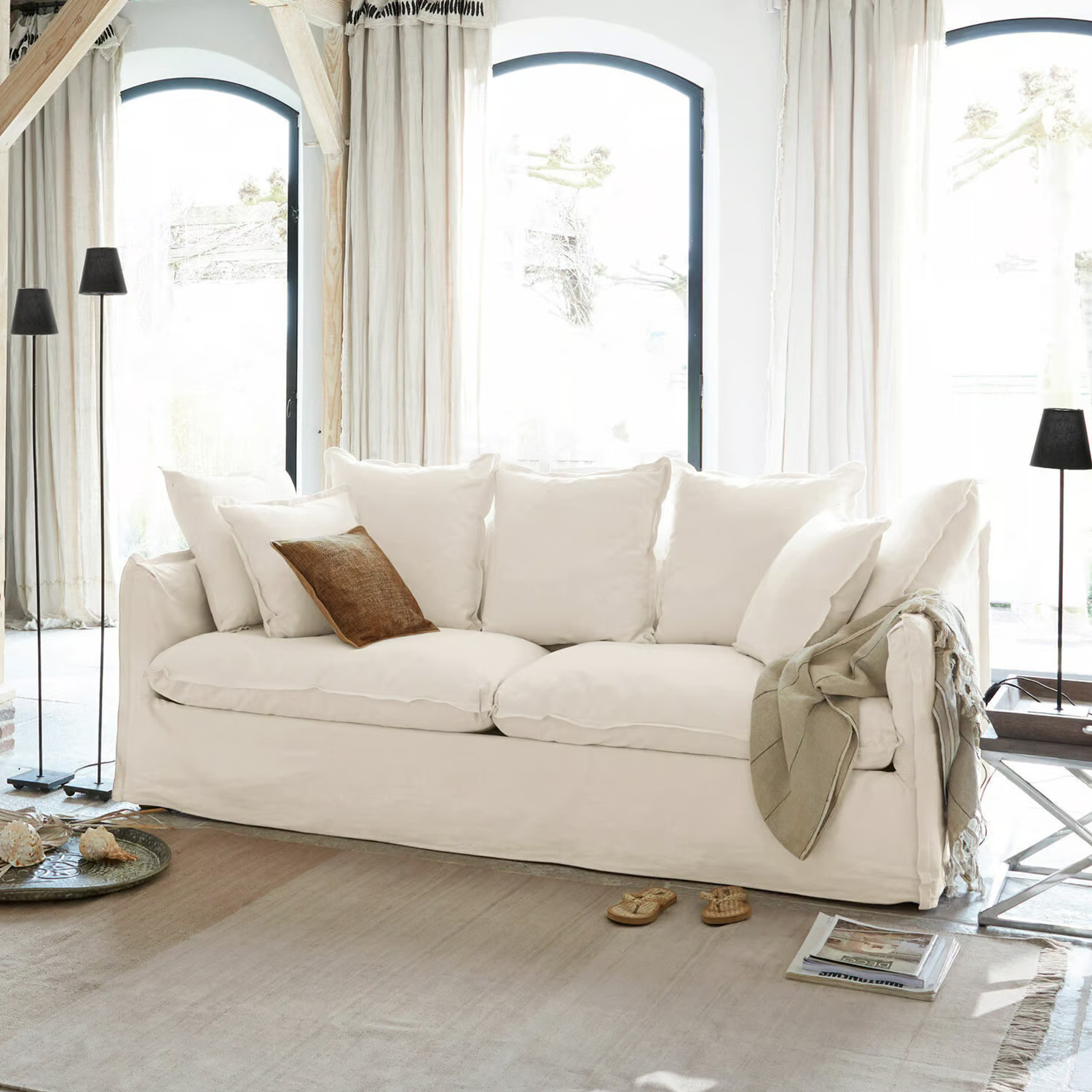 Grand canapé blanc en coton avec coussins et coussin décoratif marron dans un salon lumineux
