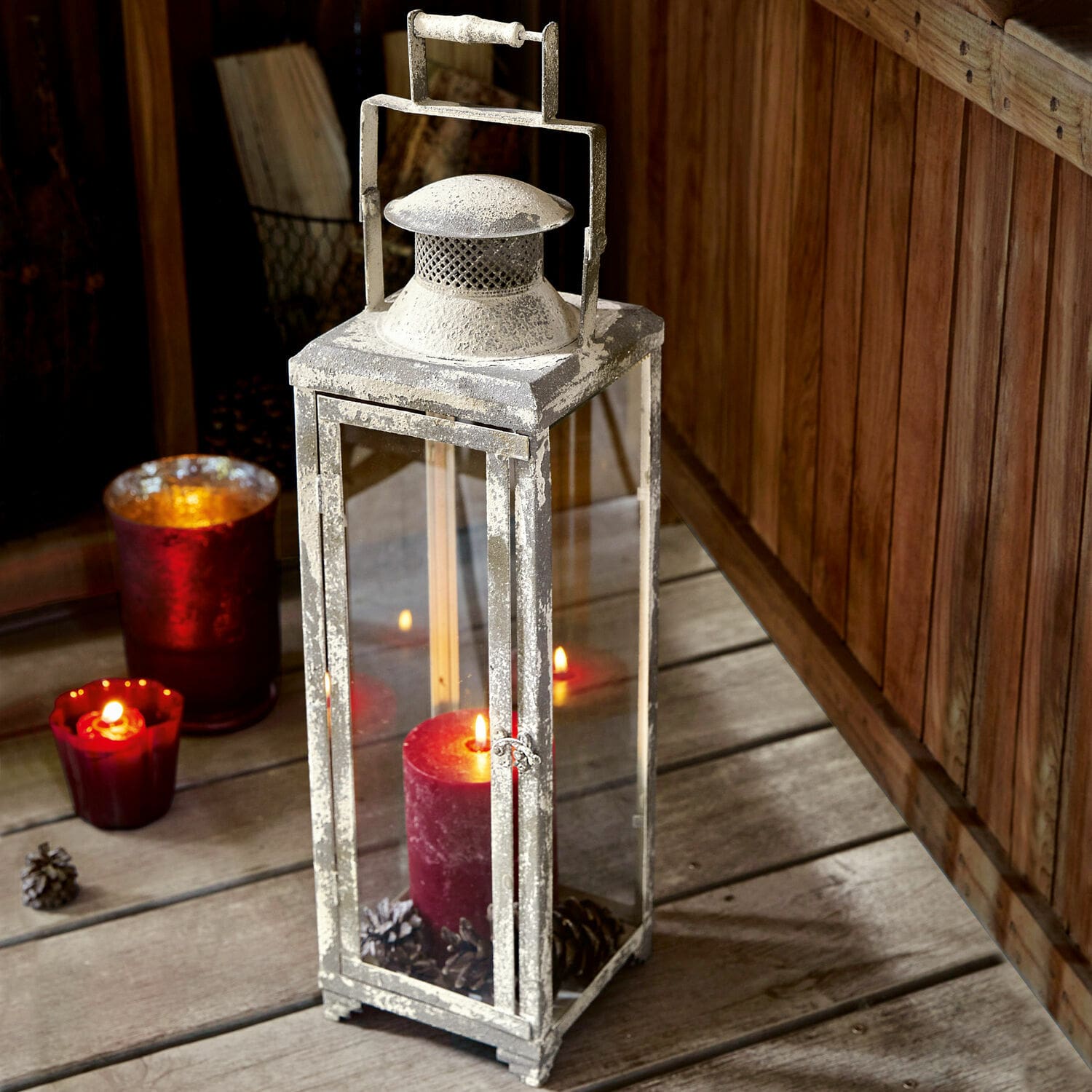 Lantaarn Isodore Metalen lantaarn in vintage stijl met witte patina en rode kaars op houten vloer