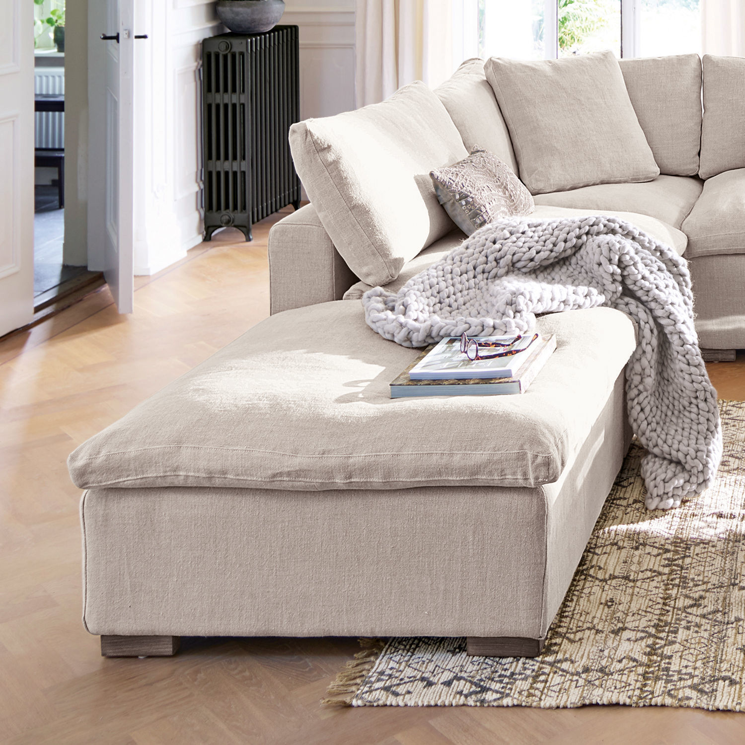 Canapé d'angle beige en tissu avec couverture douce et coussins dans un salon lumineux au sol en bois