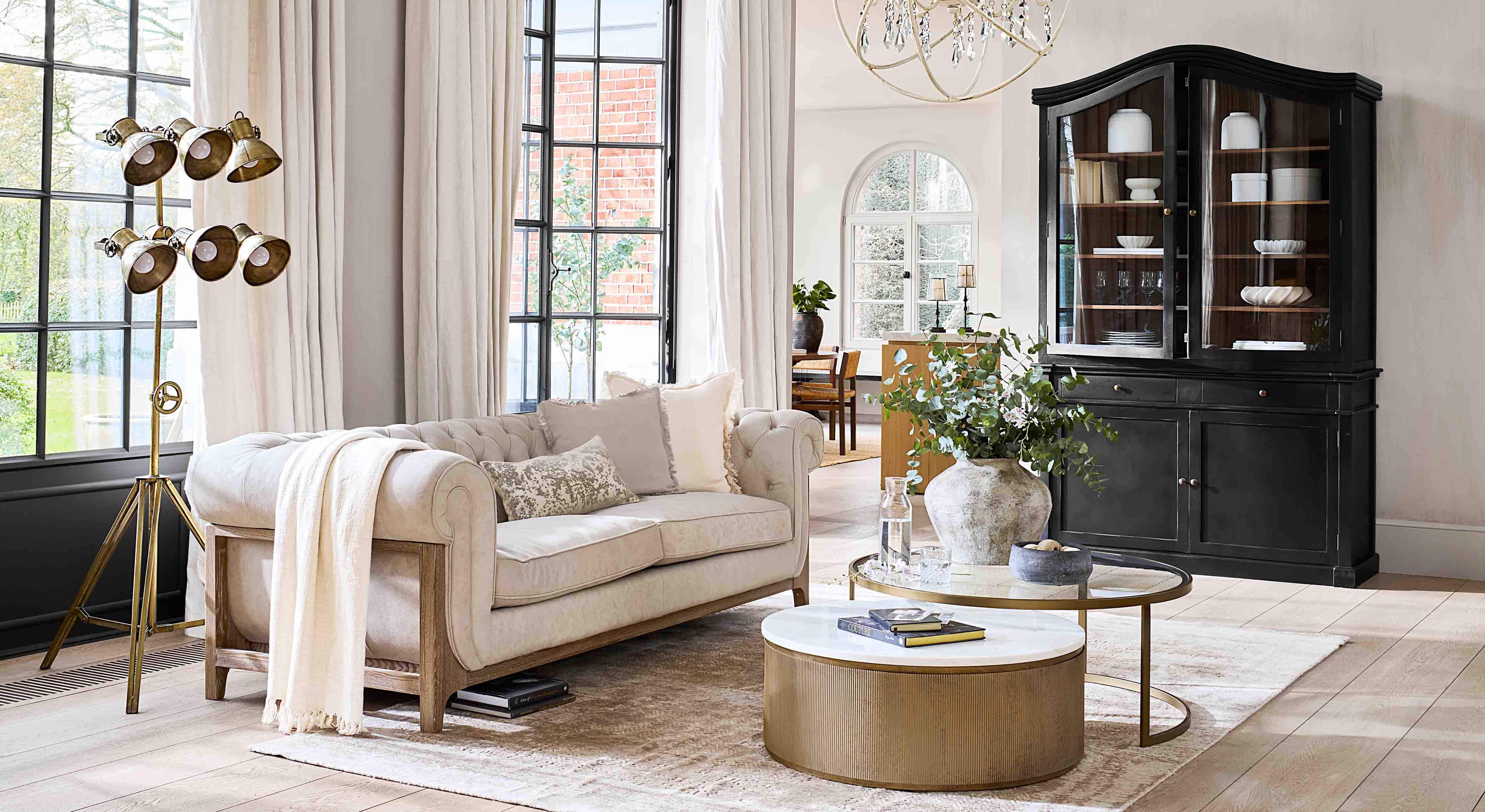 Canapé beige avec cadre en bois dans un salon lumineux avec vitrine noire et lampe dorée