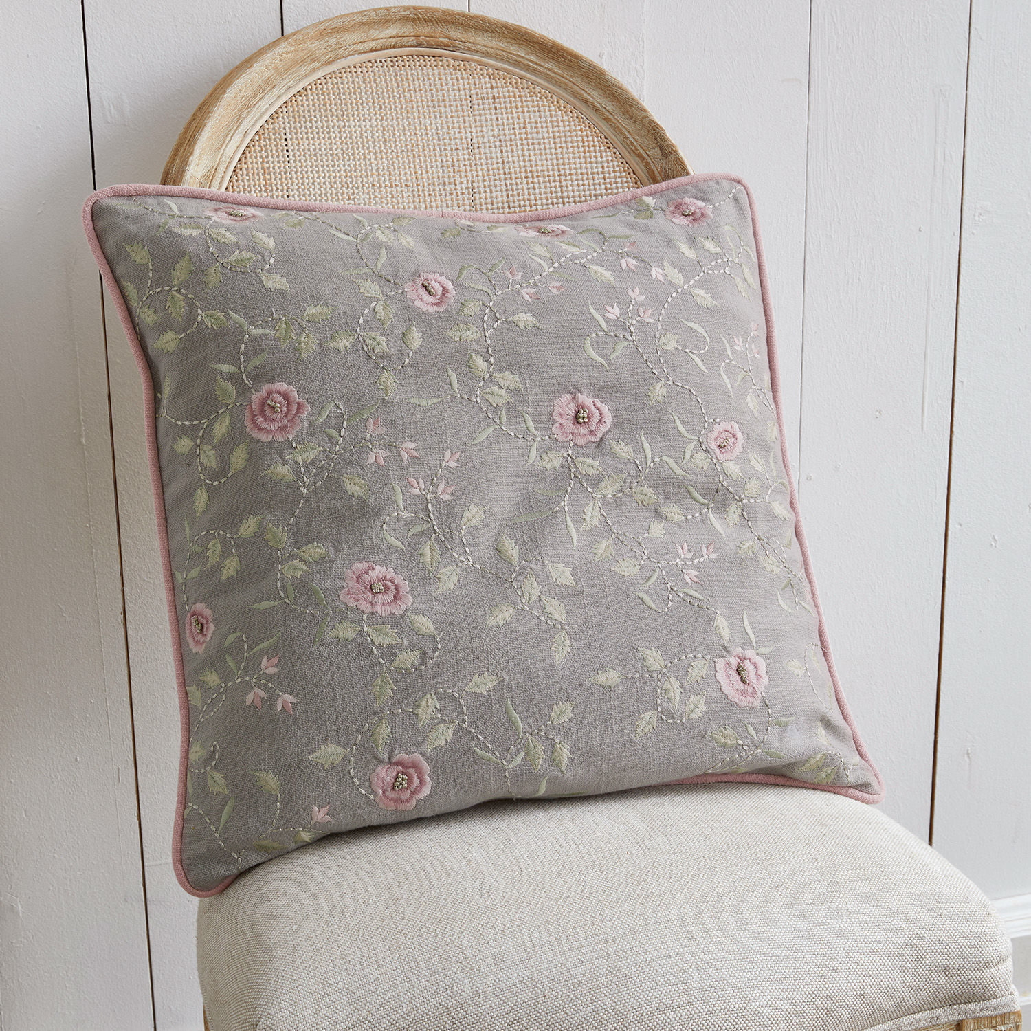 Coussin décoratif gris avec broderie florale rose sur chaise beige, textile d'intérieur élégant