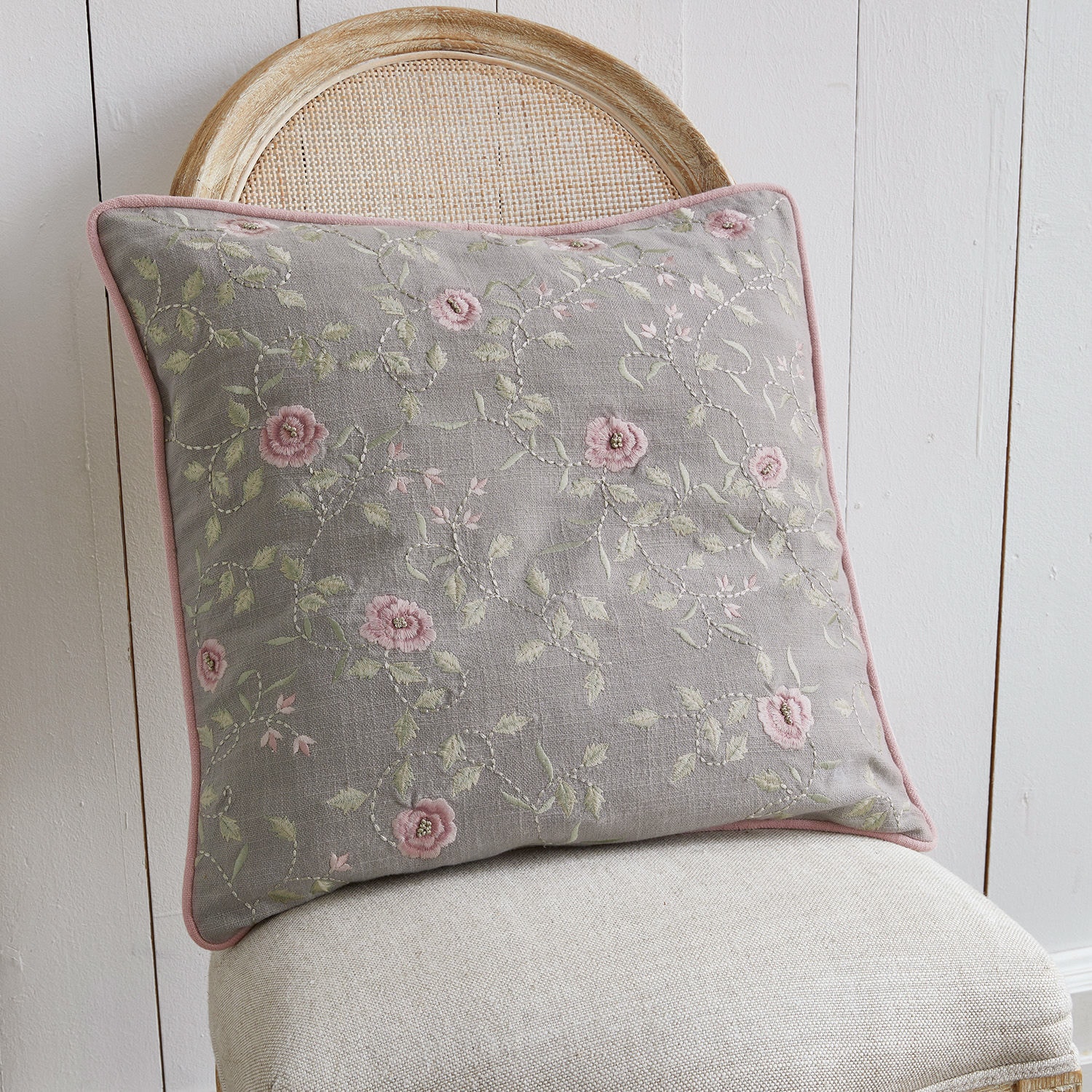 Coussin Rosalena Coussin décoratif gris avec broderie florale rose sur chaise beige, textile d'intérieur élégant