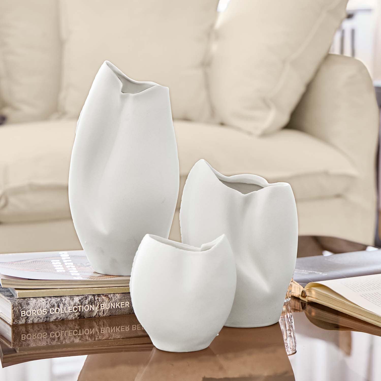 Ensemble de trois vases en céramique blanche aux formes irrégulières posés sur une table avec des livres