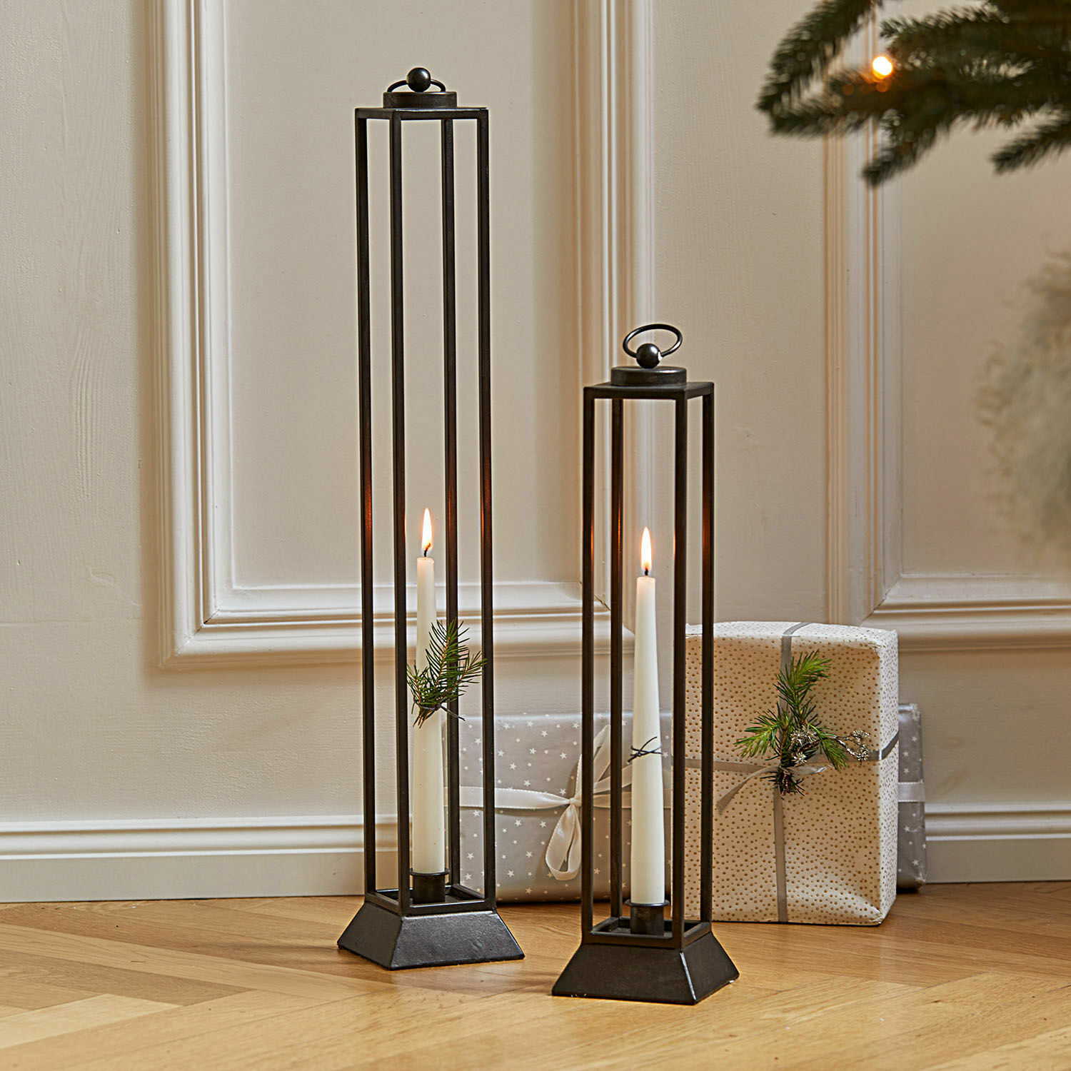 Lot de 2 lanternes Régat Deux lanternes en métal noir avec bougies blanches et décorations de branches sur parquet en bois