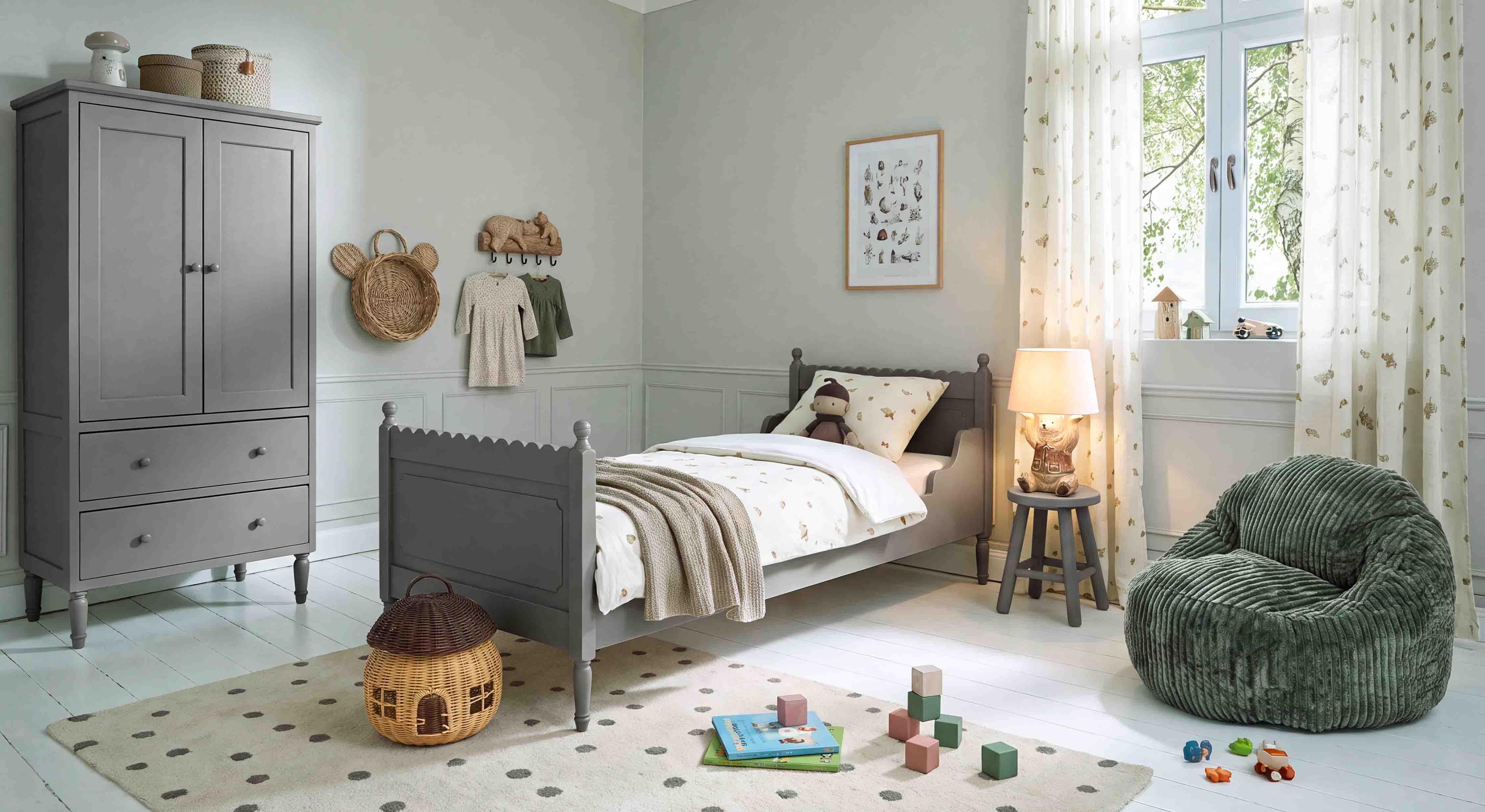 Armoire et lit en bois gris dans une chambre d'enfant avec fauteuil vert doux et décorations