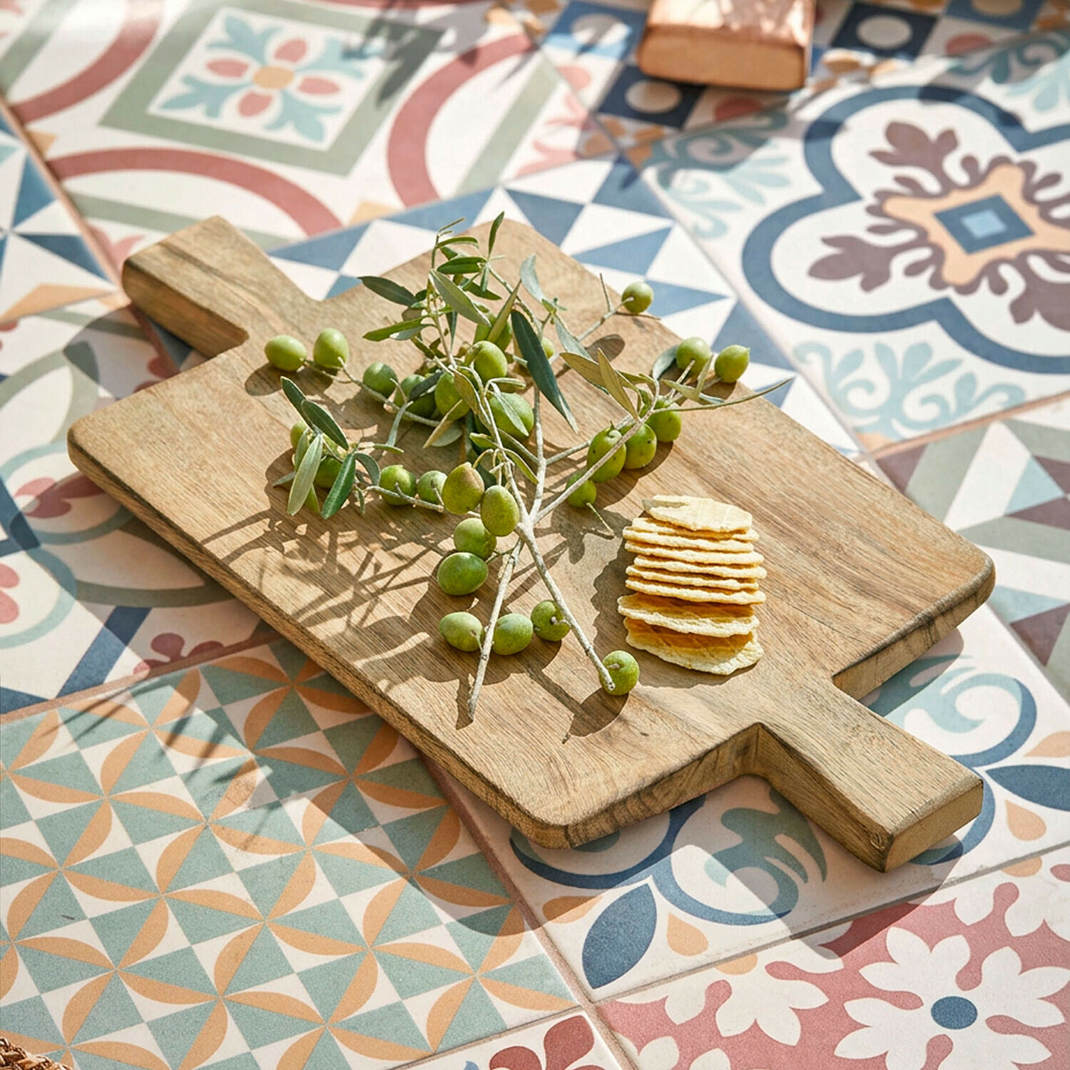 Planche à découper en bois avec olives vertes et crackers sur un sol en mosaïque colorée
