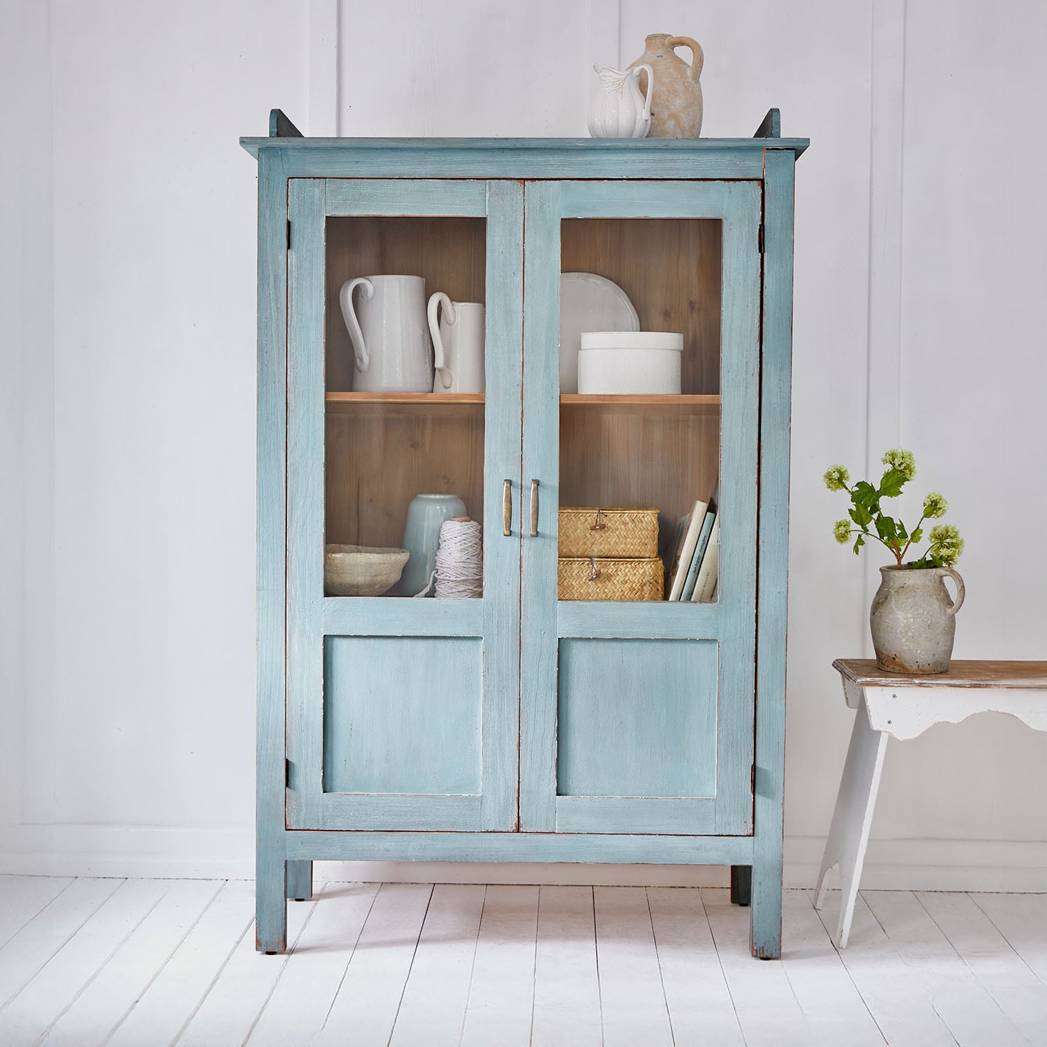 Armoire en bois bleu avec portes vitrées et décorations en céramique style vintage dans une pièce claire