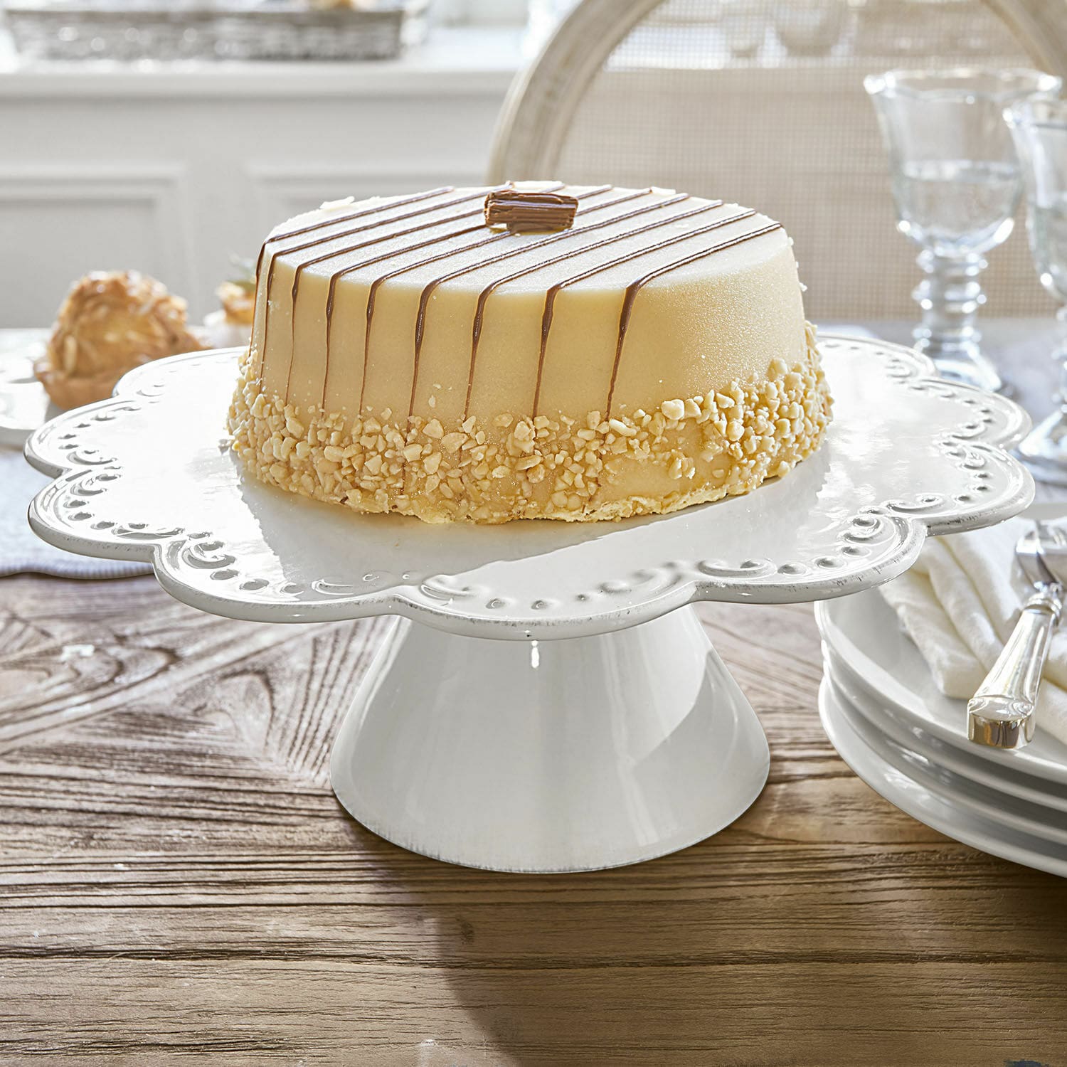 Plat à gâteau Fontienne Présentoir à gâteau en céramique blanche avec bord décoratif sur table en bois dans une salle à manger
