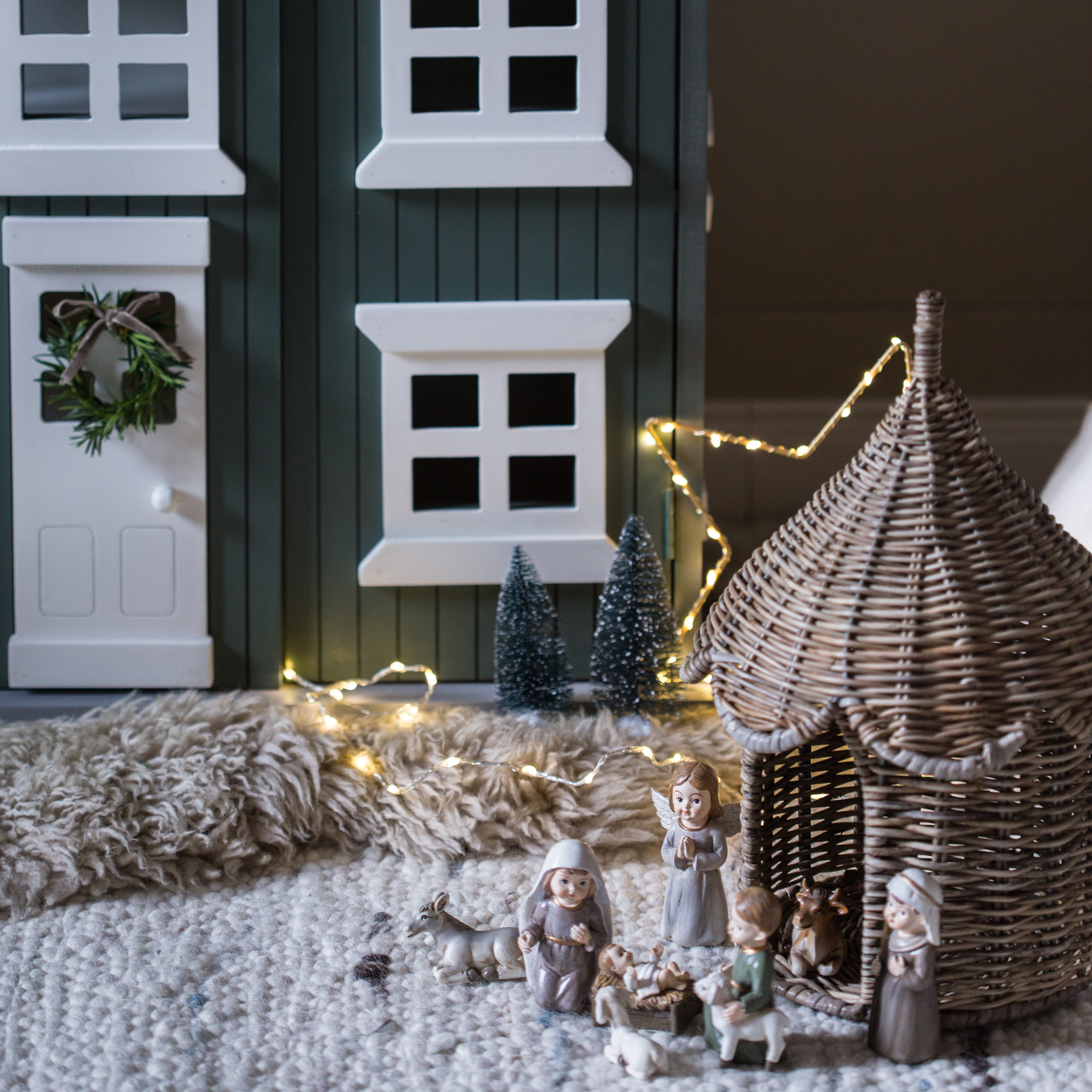 Décoration de Noël avec figurines de crèche et étable en osier sur tapis avec guirlande lumineuse