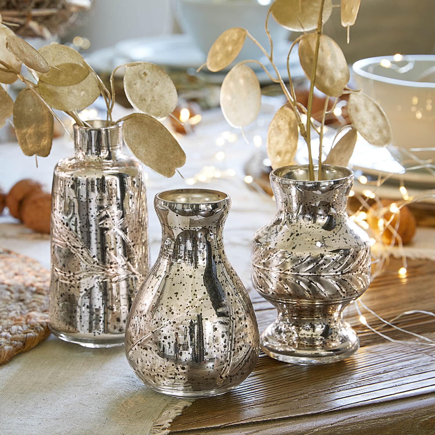 Ensemble de trois vases argentés avec finition métallique et décor de feuilles sur une table en bois