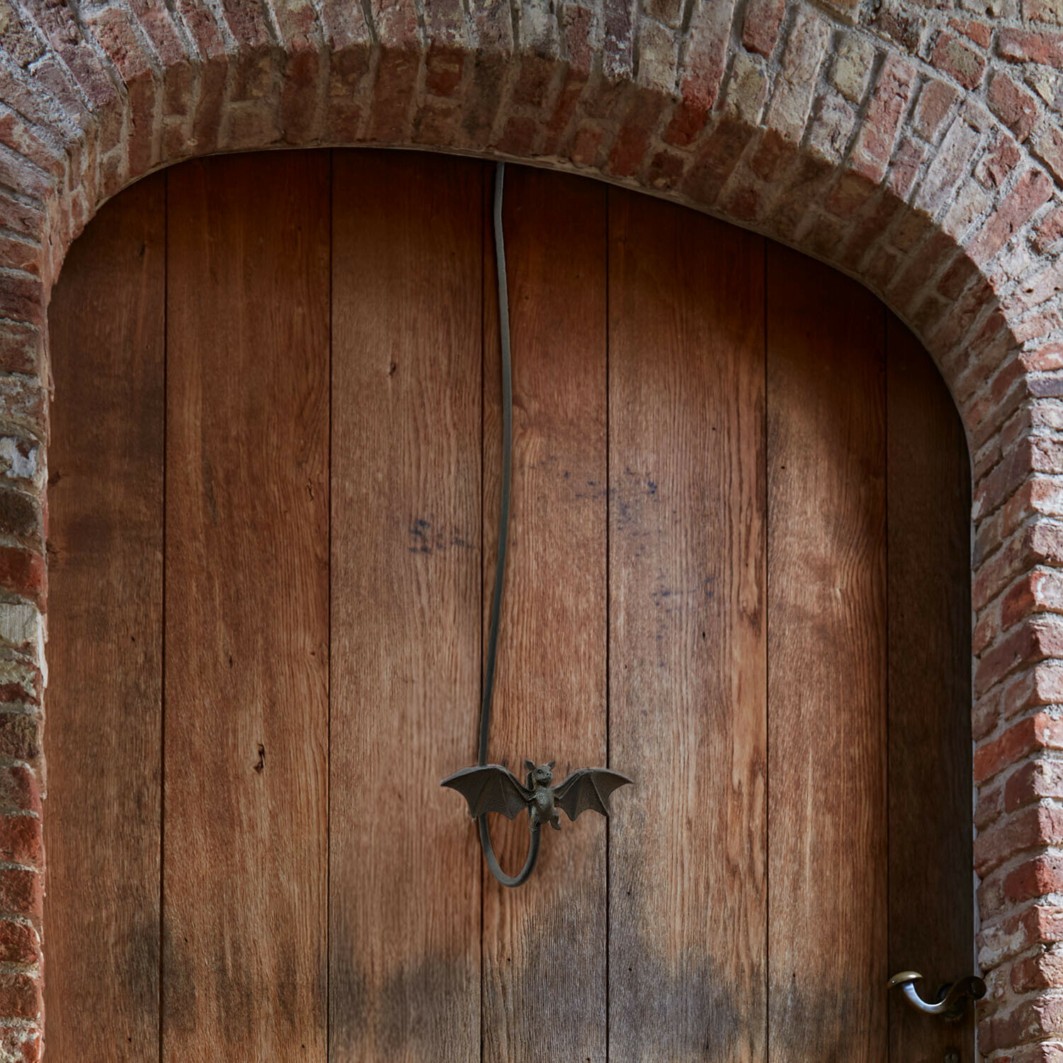 Houten deur met bakstenen boog en metalen vleermuisvormige handgreep in vintage stijl