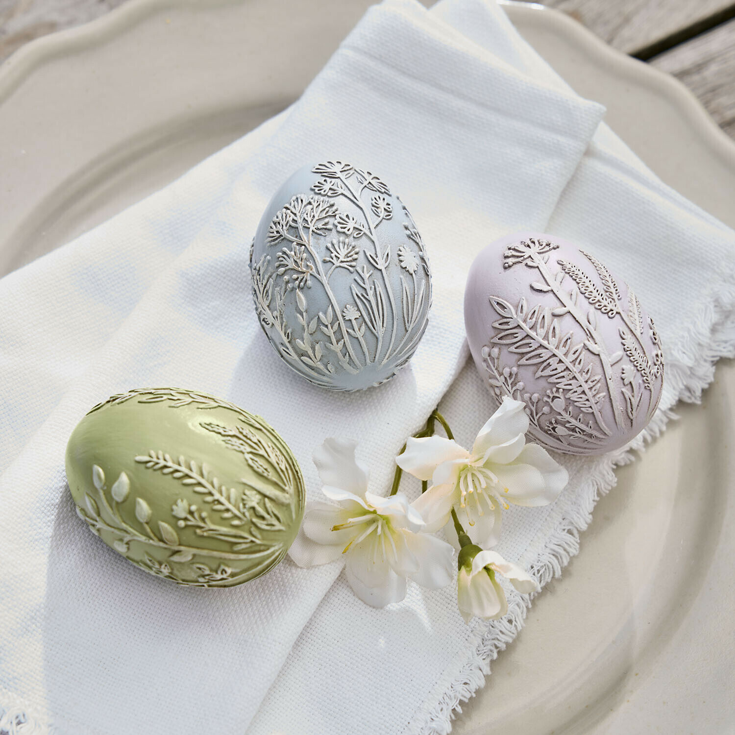 Paasei set van 3 Fauverine Drie pastelgekleurde decoratieve eieren met reliëf van planten op witte stof en bloemen op bord